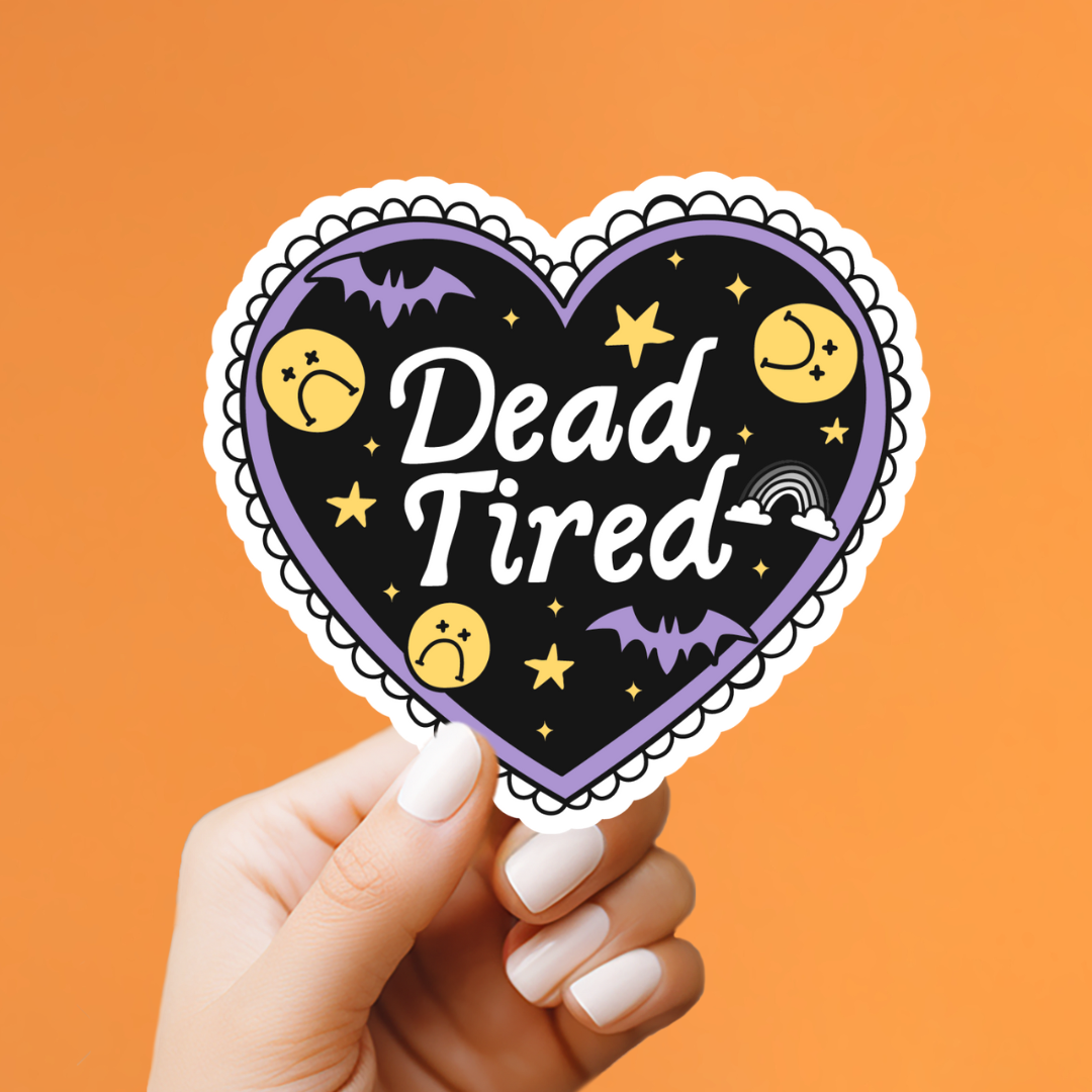 A hand with white manicured nails holds a heart-shaped sticker against a solid orange background. The sticker features a black background with the words &