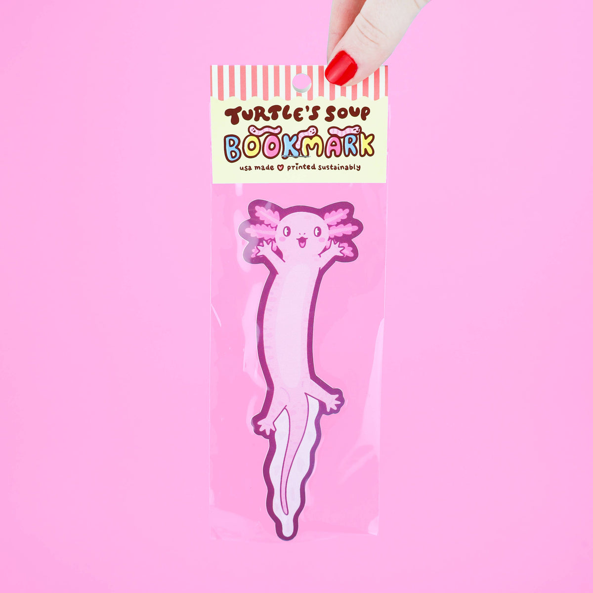 Bookmark with cartoon axlotl design held by a hand against a pink background