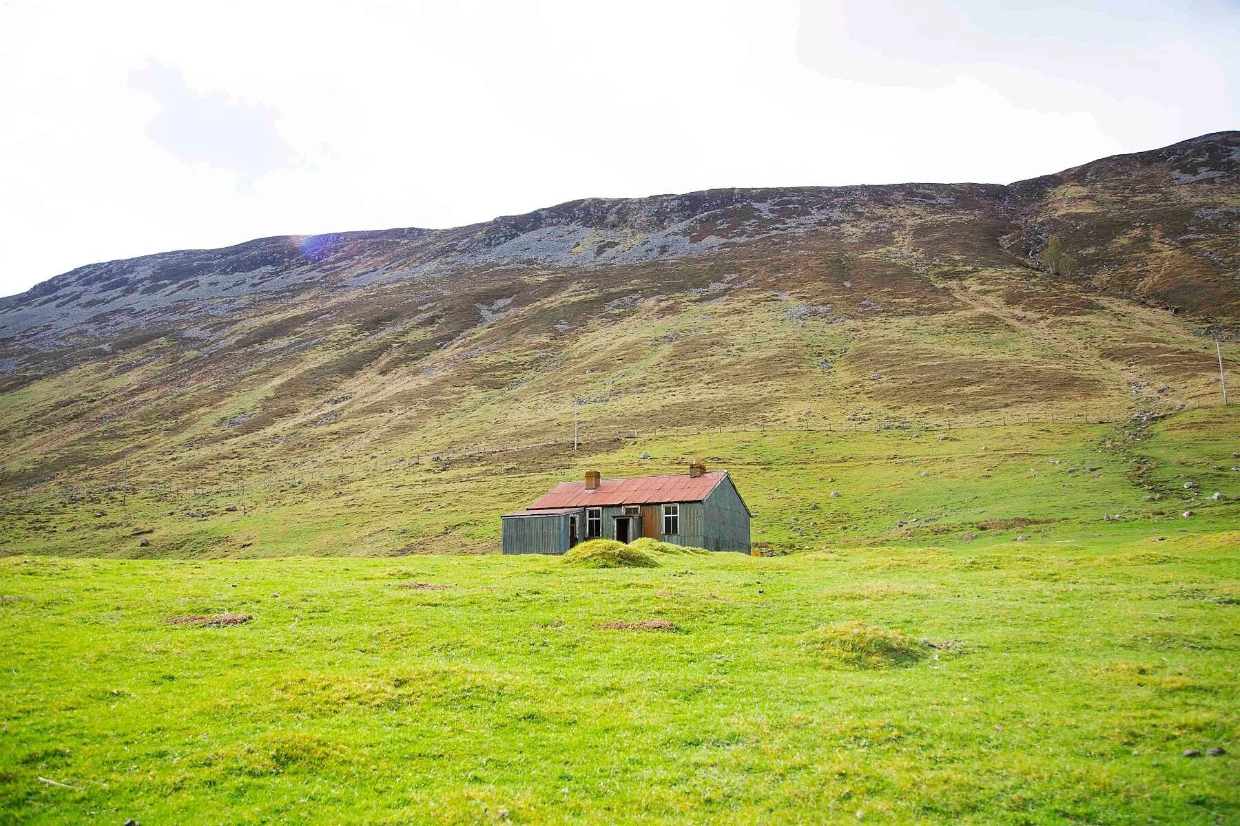 Photograph of an abandoned house in the green hills of a glen in Scotland.