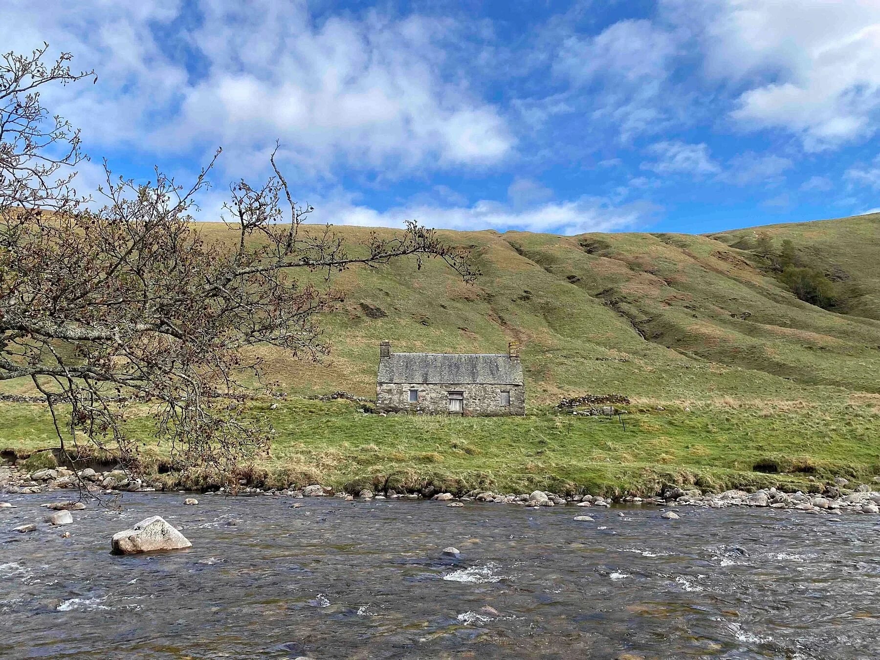 Photograph of a stone cottage under a bright blue sky on the bank of the River Tilt in Scotland.