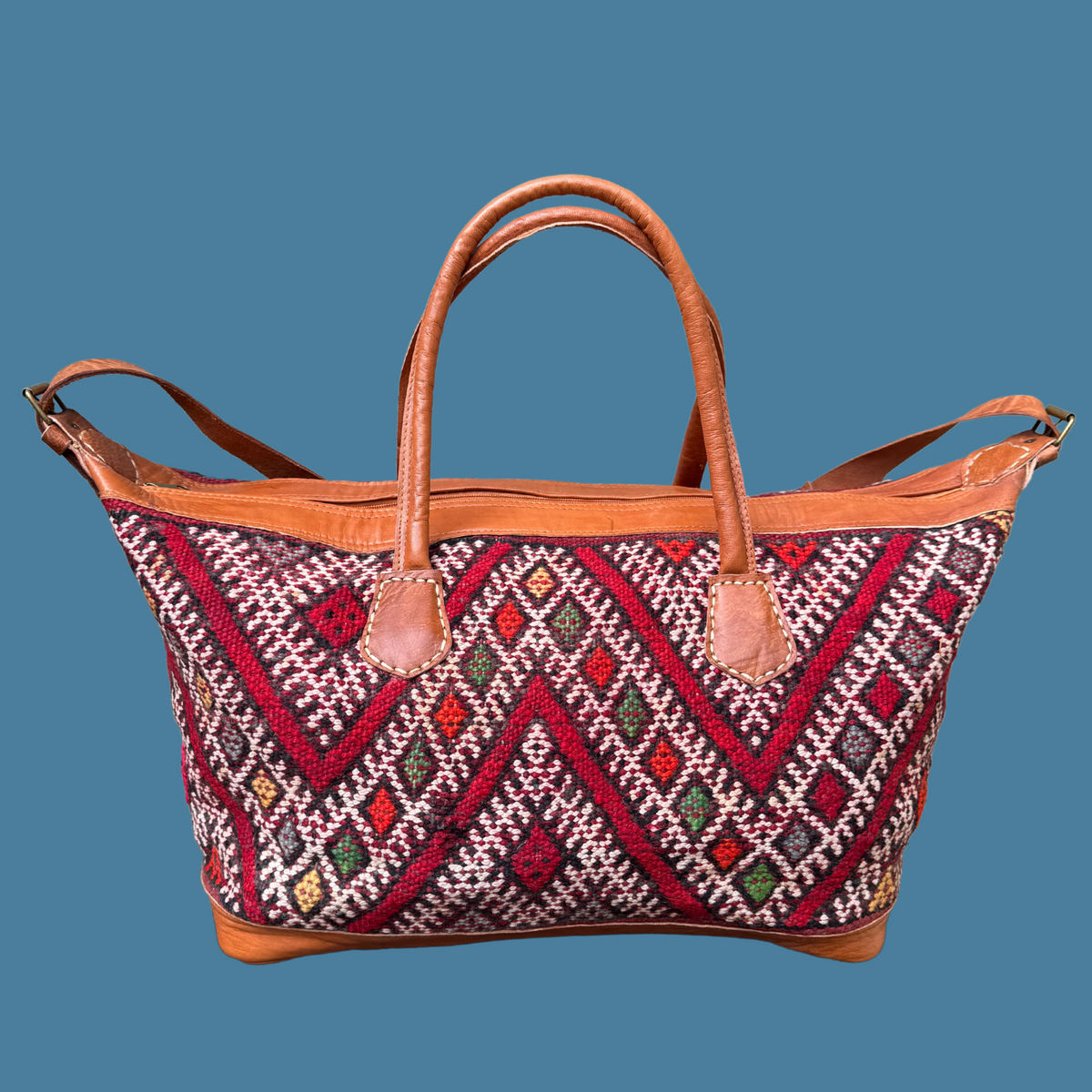 Kilim Weekender with intricate pattern and brown handles on a blue background
