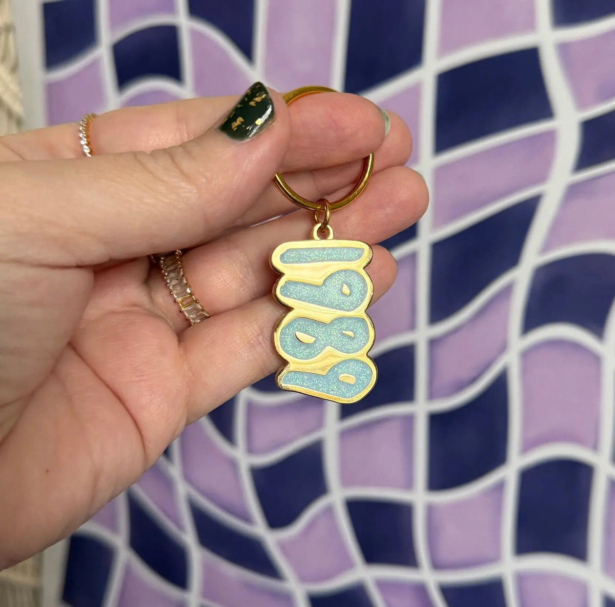 1989 blue glitter enamel keychain detail — close up of the light blue glitter enamel lettering by indie artist MangoIllustrated