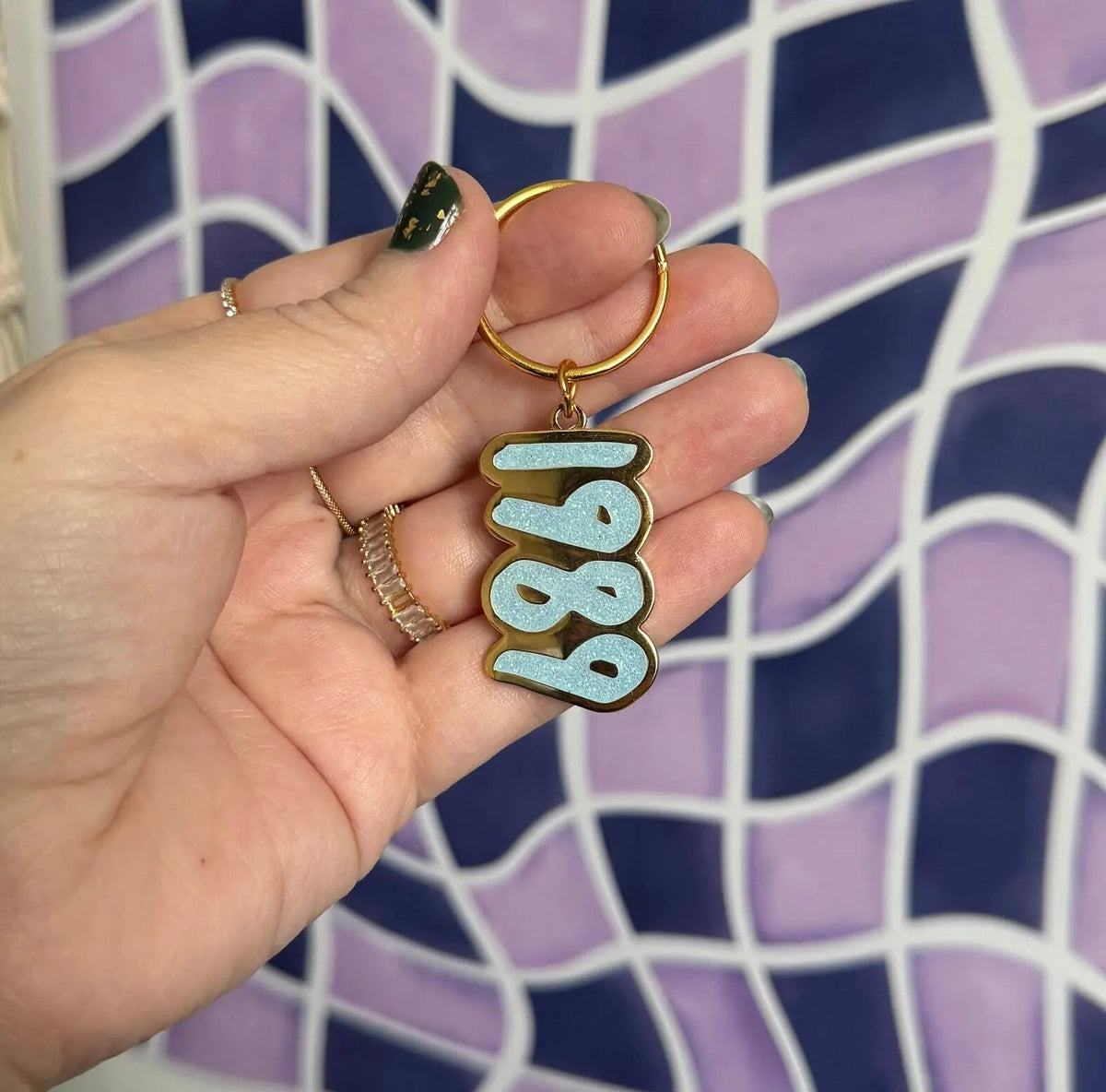 1989 blue glitter enamel keychain flat lay — glitter enamel keyring on a split ring by indie artist MangoIllustrated