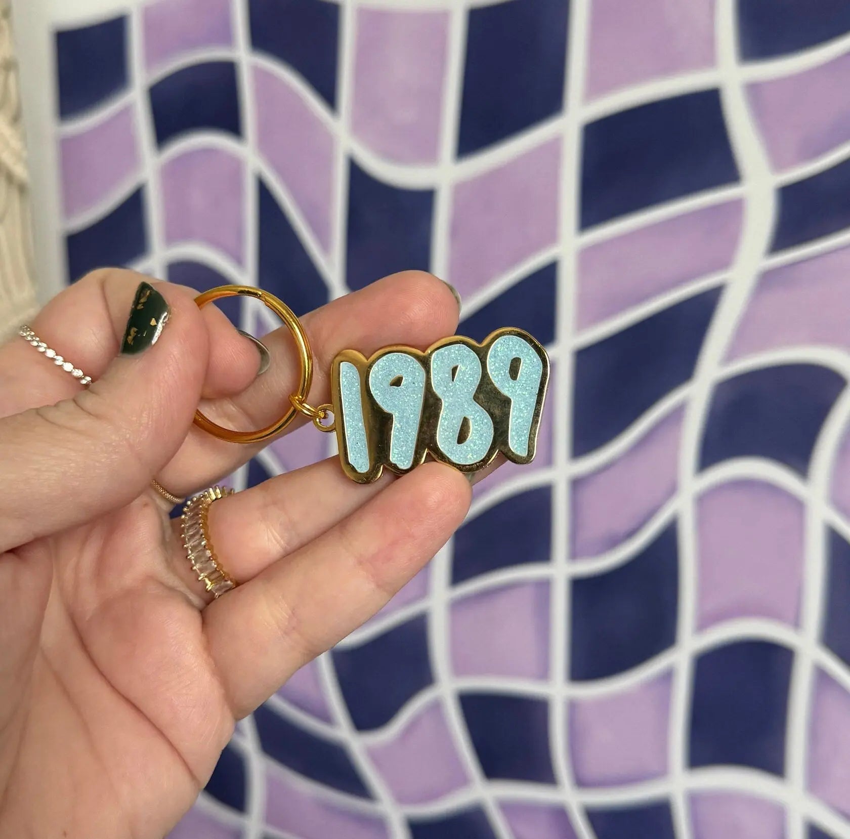 1989 blue glitter enamel keychain scale view — 1.5 by 1 inch glitter enamel bag charm by indie artist MangoIllustrated