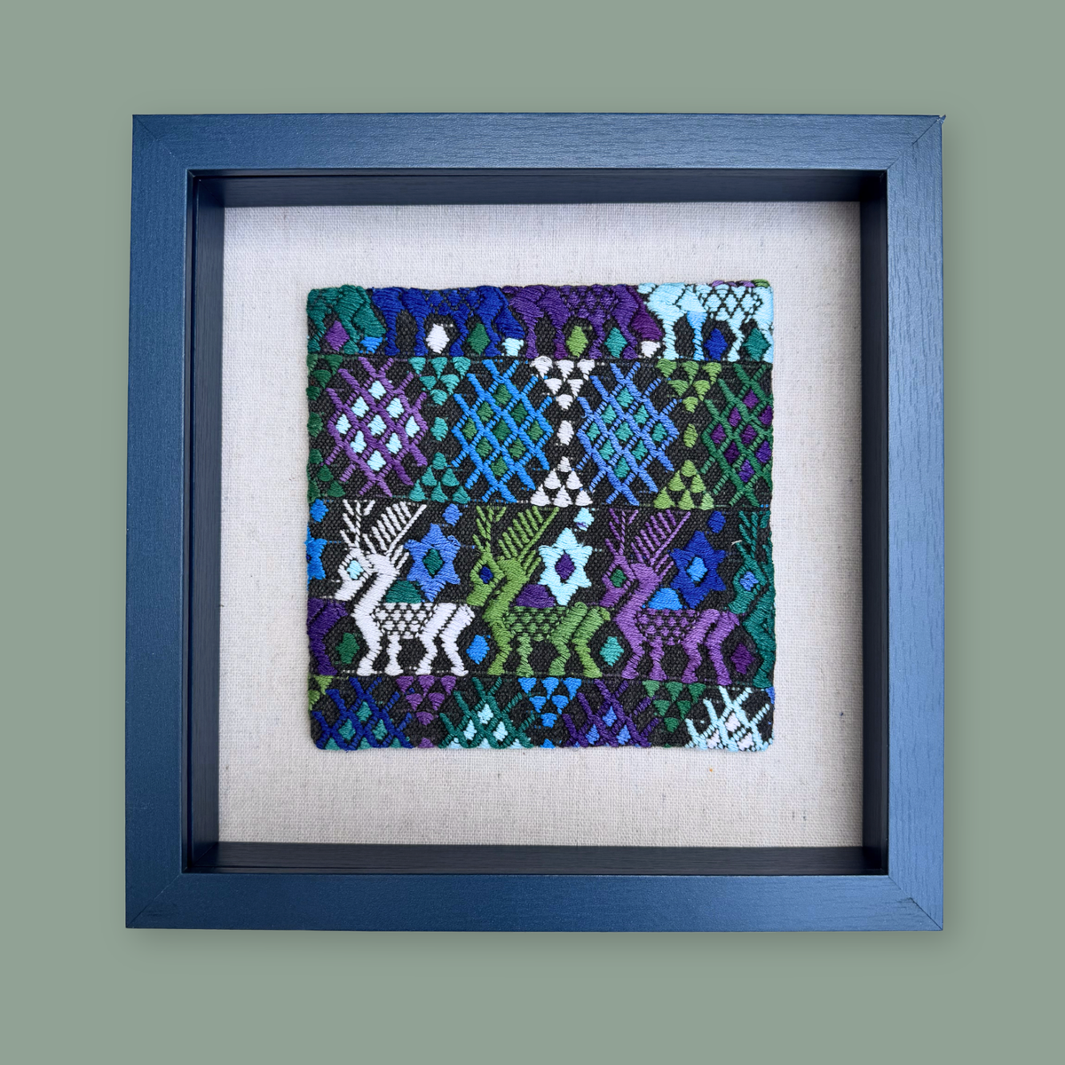 Framed textile art piece with geometric patterns and deer designs on a gray background