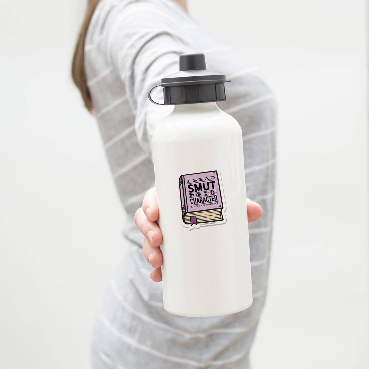 Person holding a white water bottle with a black cap and a sticker on a light gray background