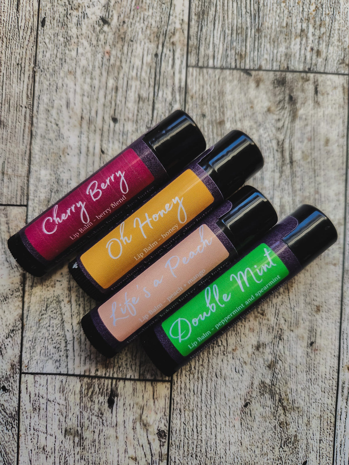 Four lip balm tubes with colorful labels on a wooden surface