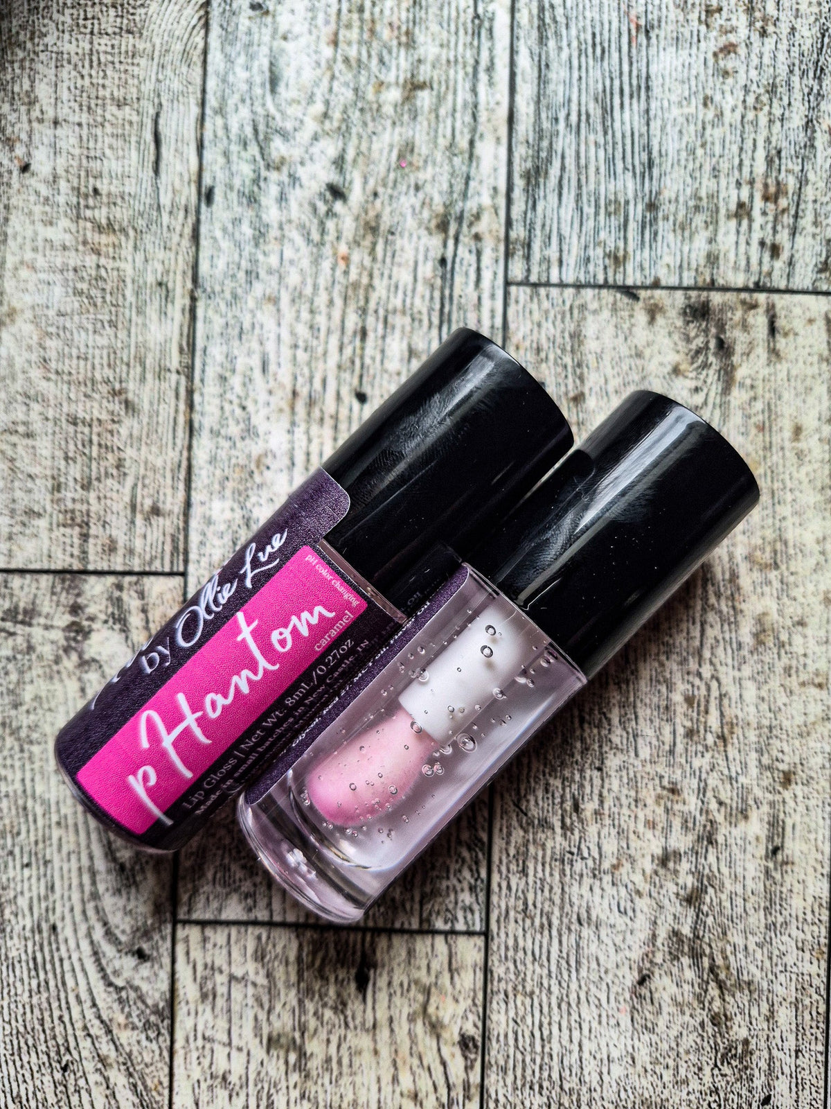 Two lip glosses with pink labels on a gray background