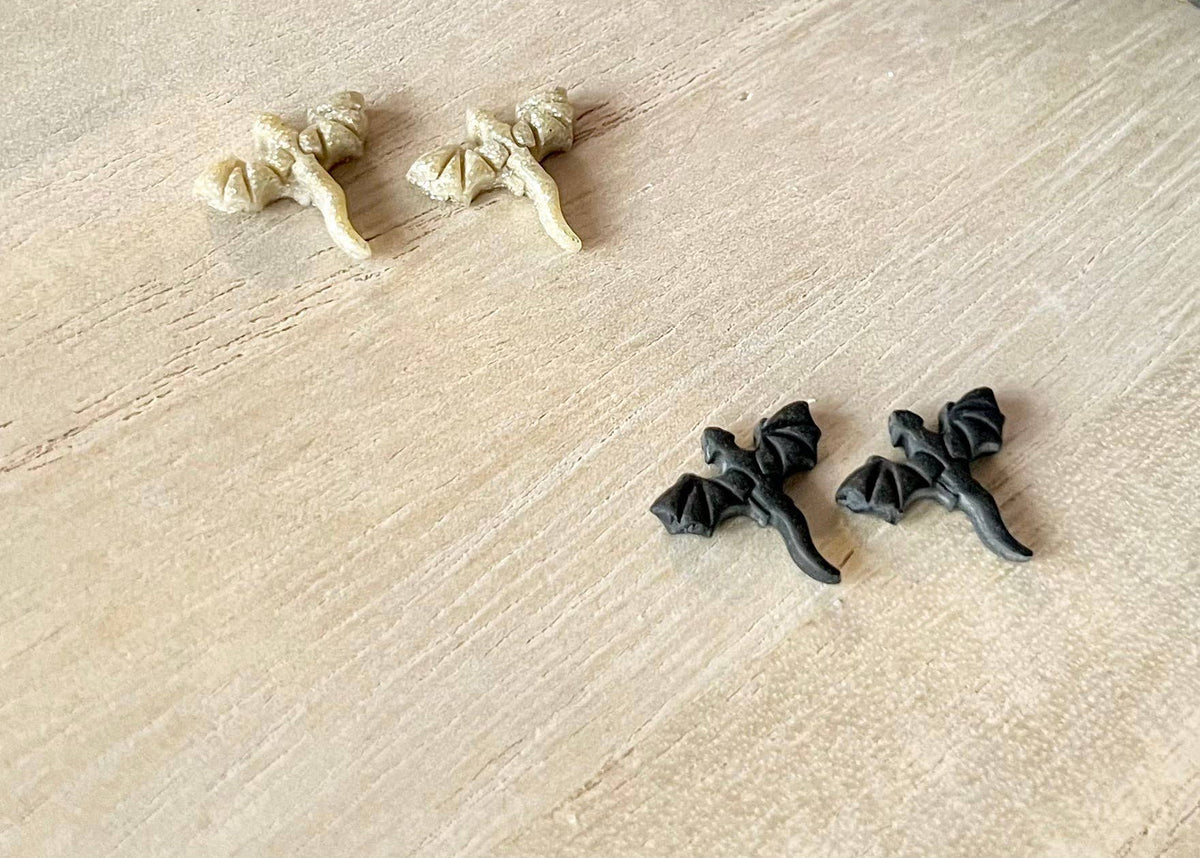 Two sets of dragon earrings on a textured beige surface
