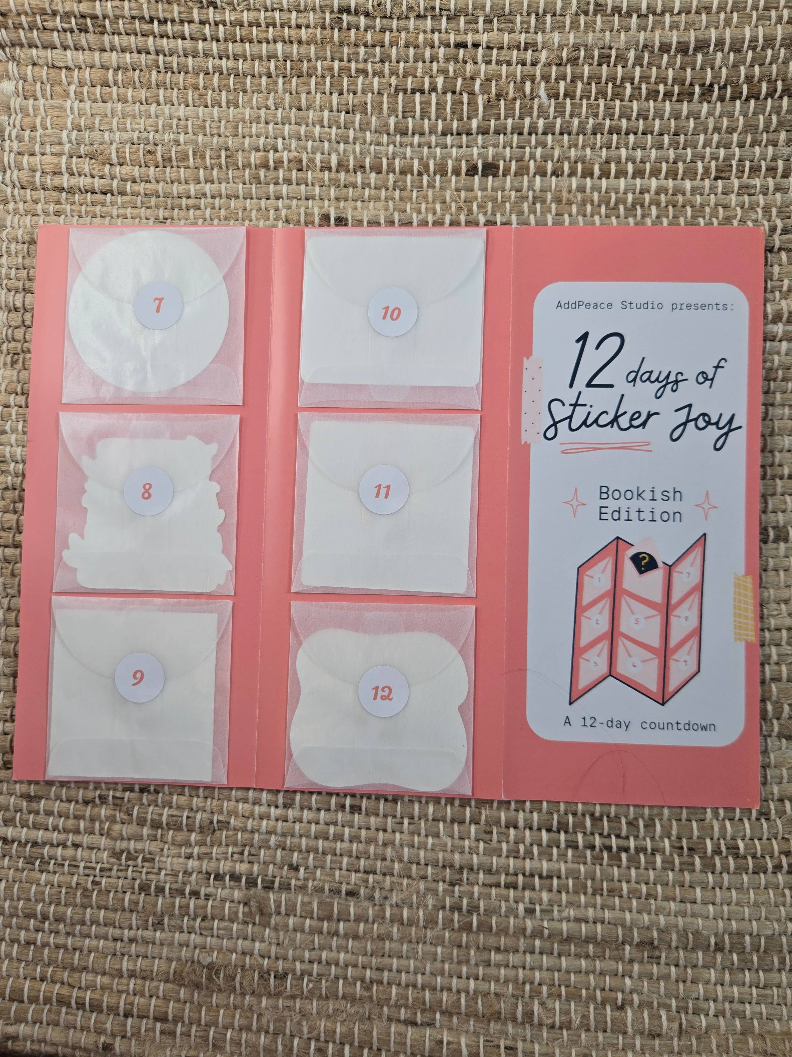12 days of Sticker Joy Bookish Edition packaging on a woven surface