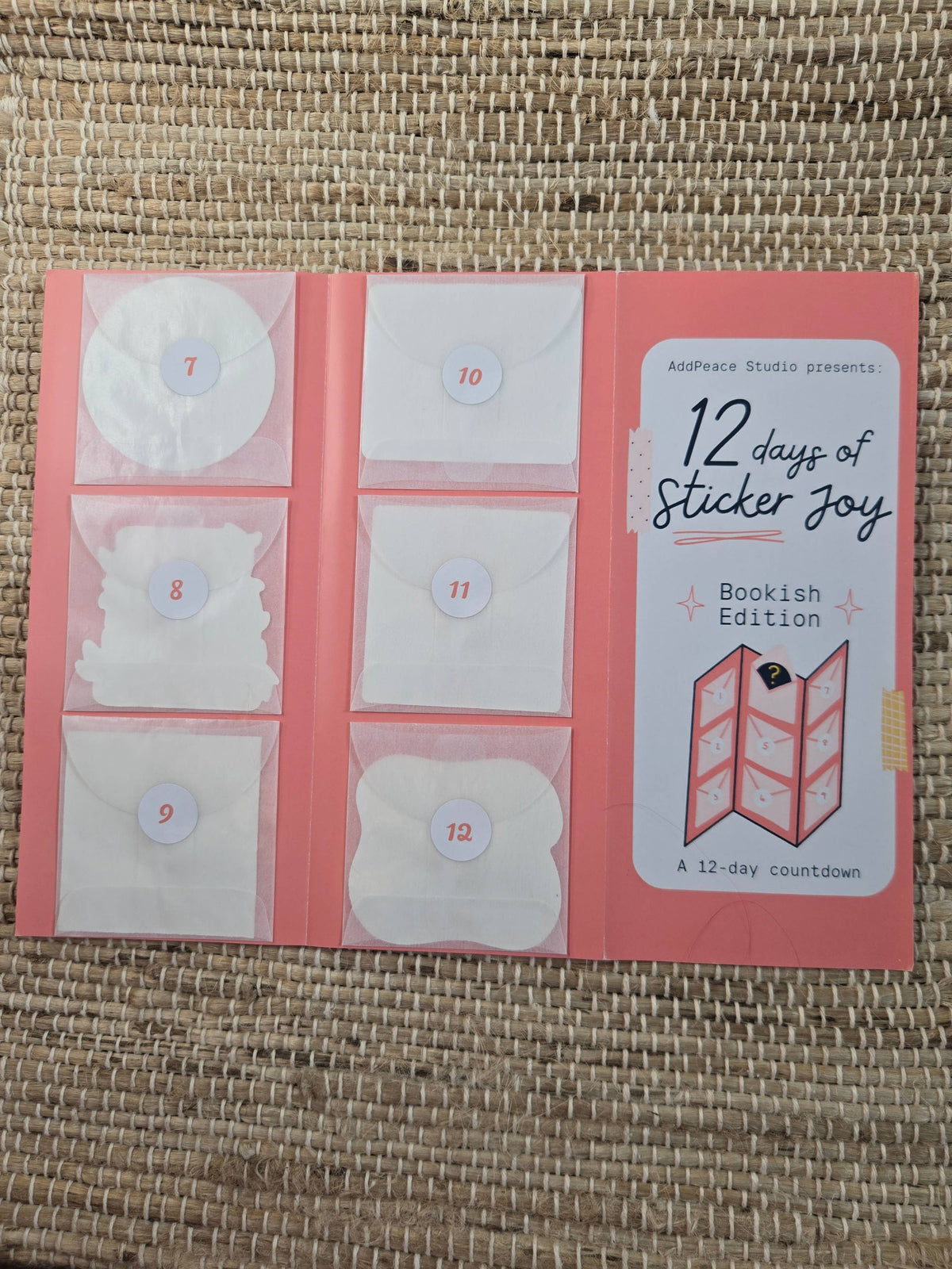12 days of Sticker Joy Bookish Edition packaging on a woven surface