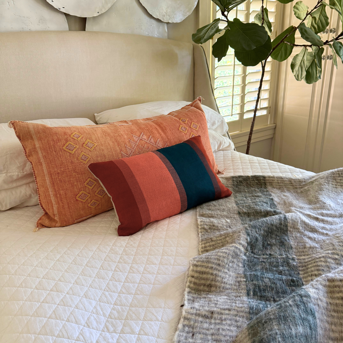 Bed with decorative pillows and a quilt, featuring a plant in the corner.