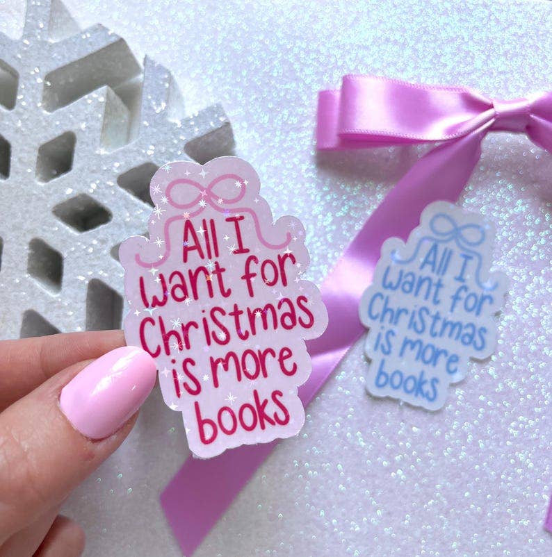 A hand with pink nail polish holds a scalloped gift box-shaped sticker that reads &