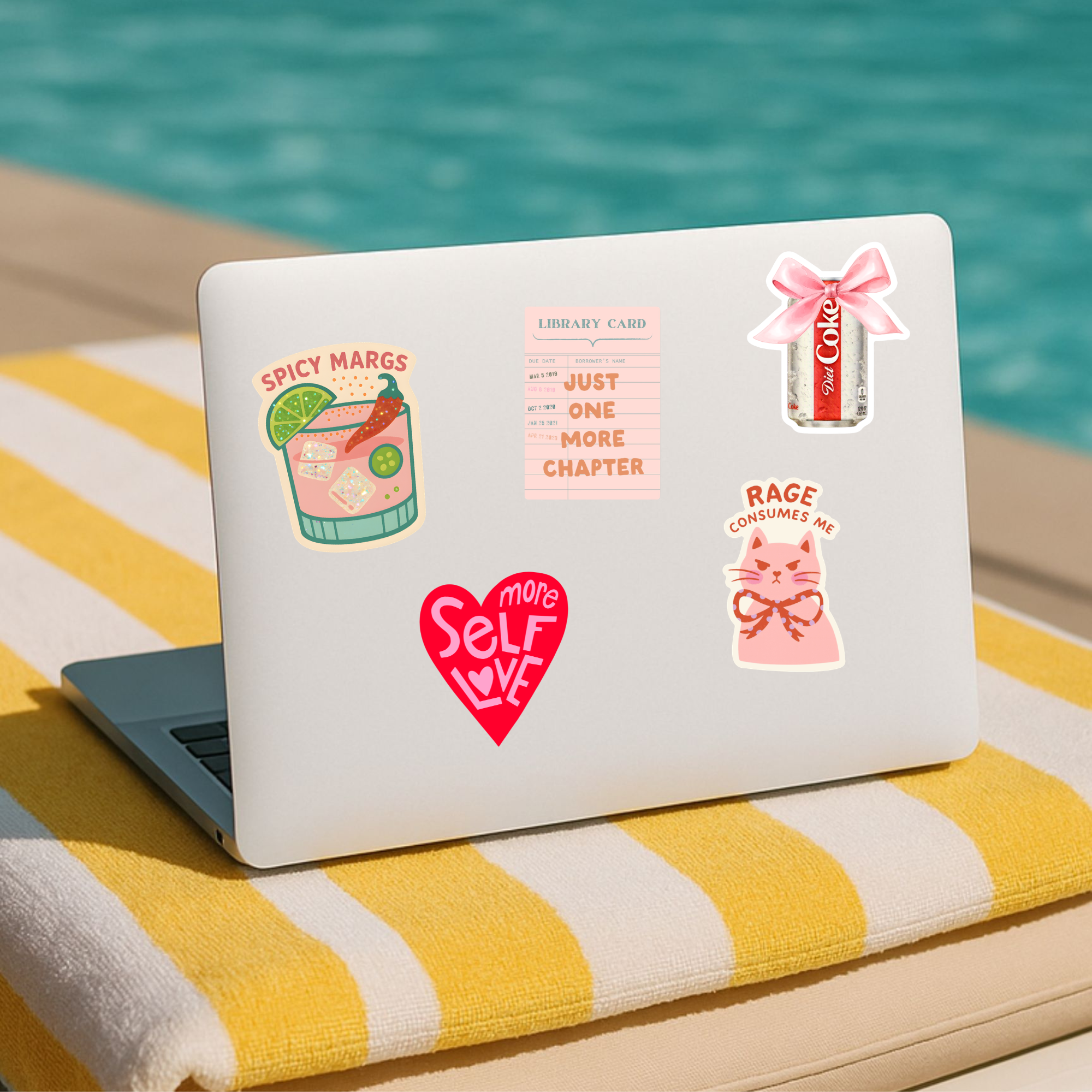Laptop with various stickers on a yellow and white striped towel by a pool.