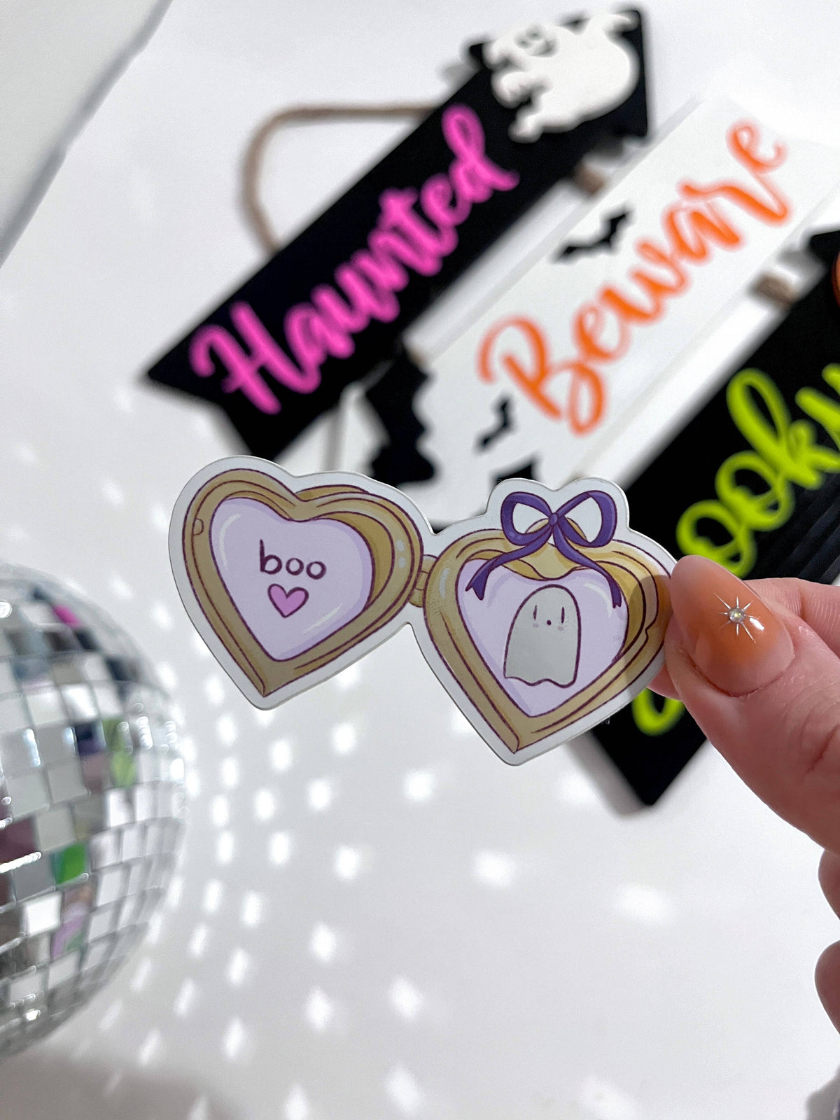 A hand holds a pair of novelty heart-shaped glasses with Halloween-themed illustrations, including one heart reading &