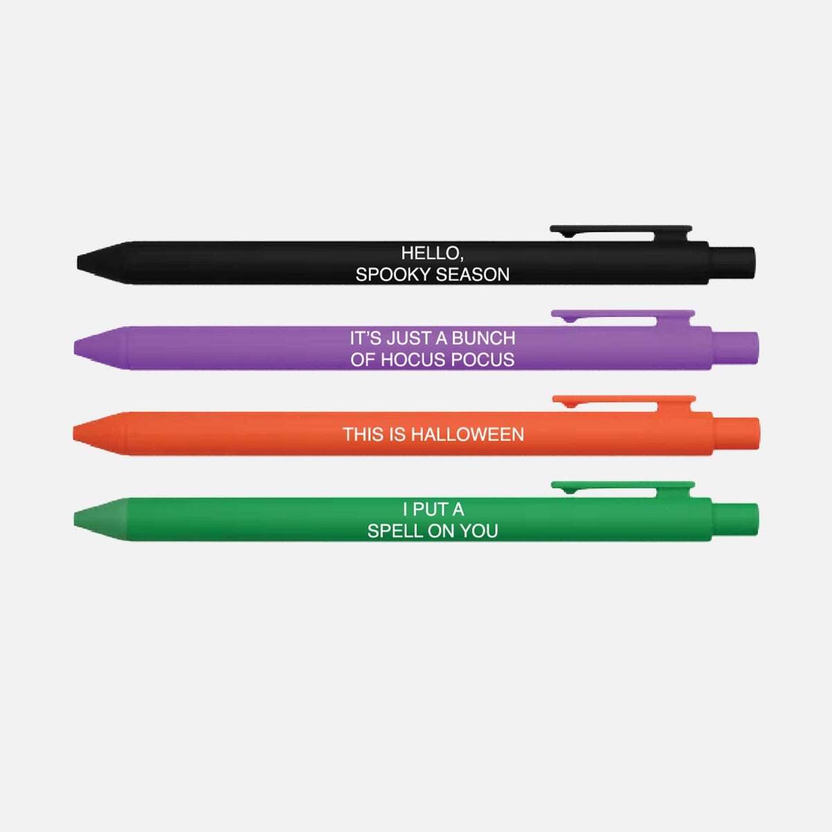 Four novelty ballpoint pens in black, purple, orange, and green, arranged vertically on a white background. Each pen has a white printed phrase related to Halloween: &