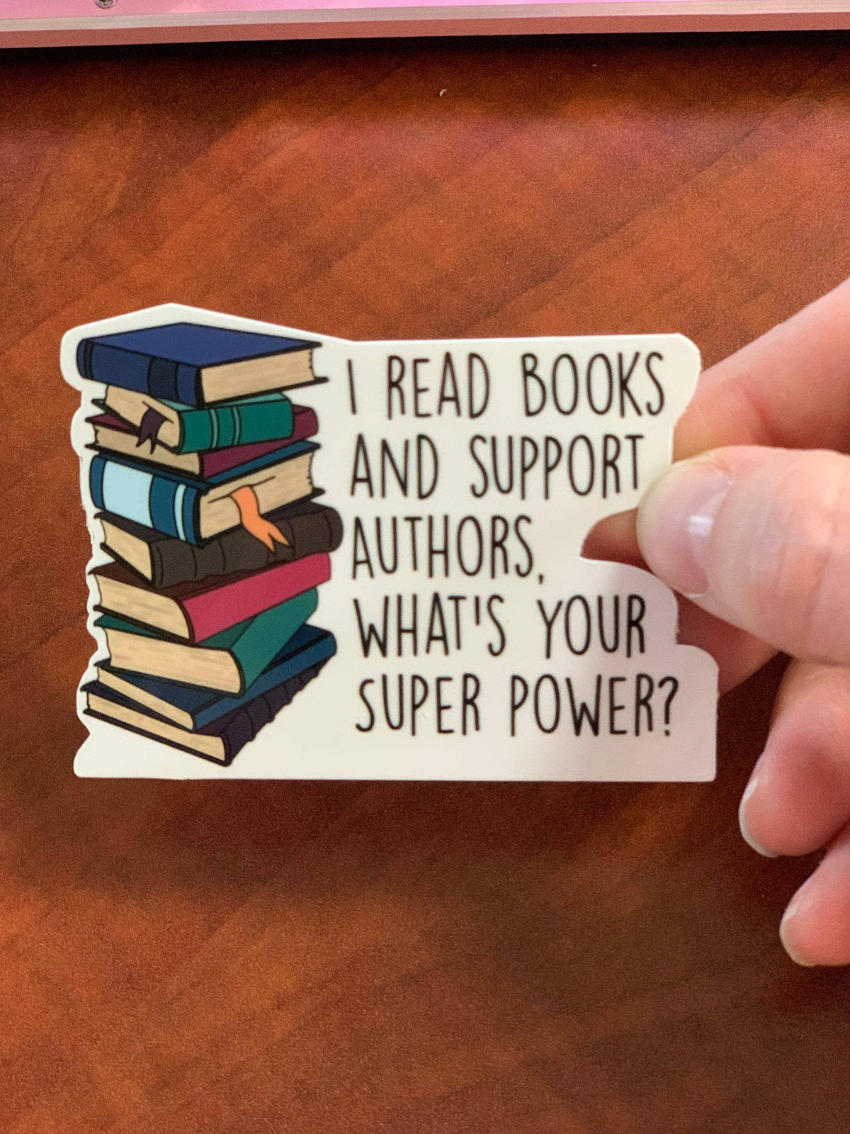 Hand holding a sticker with books and text on a wooden surface