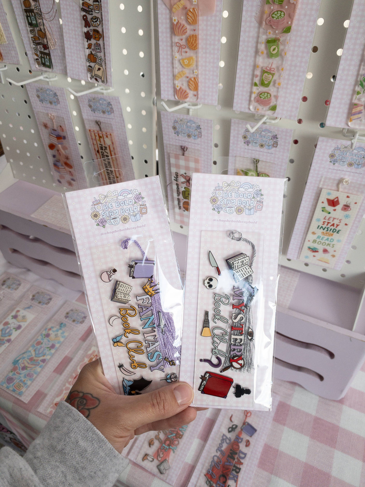 Two packages of decorative bookmarks held in front of a display of similar products.