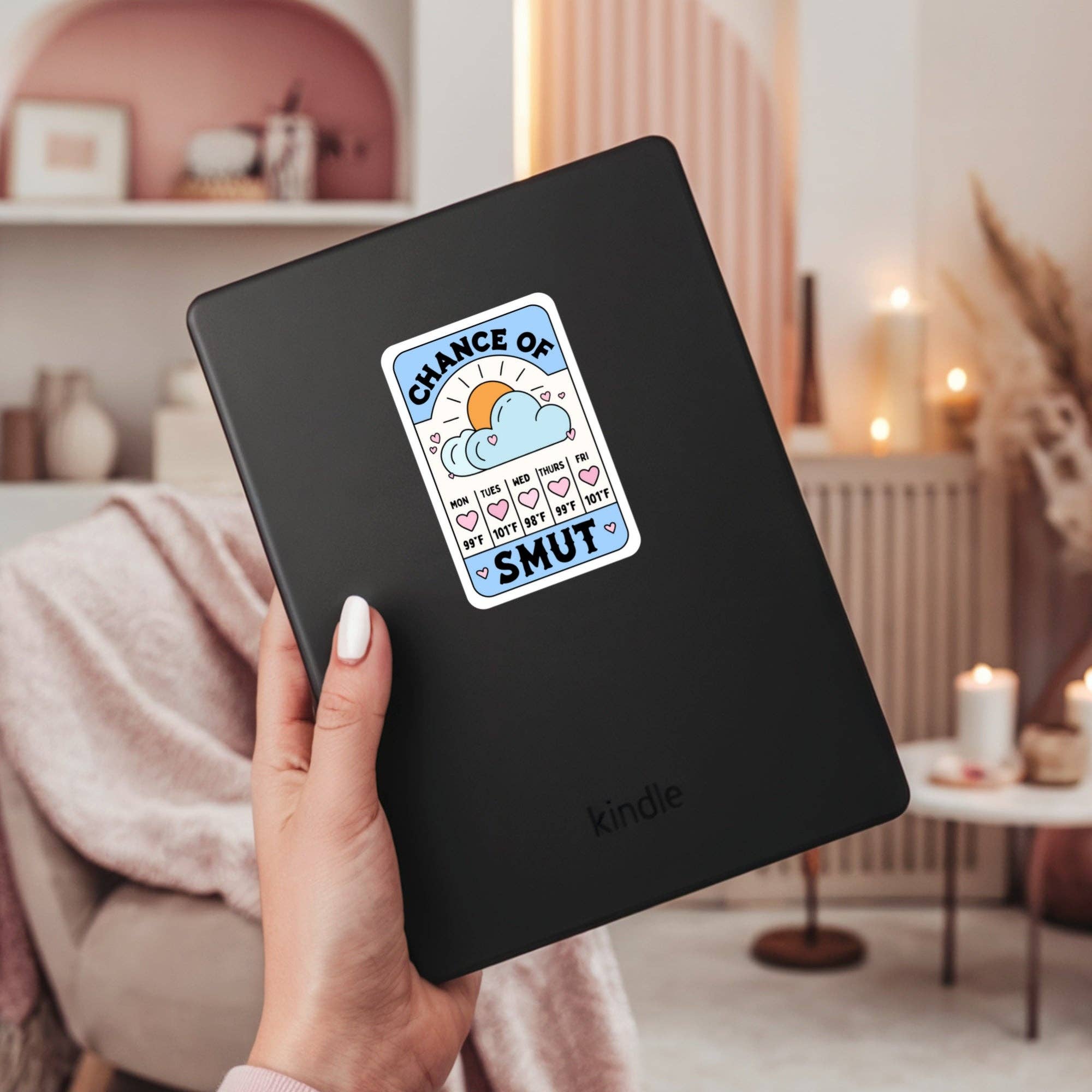 Person holding a black Kindle with a sticker on a blurred indoor background