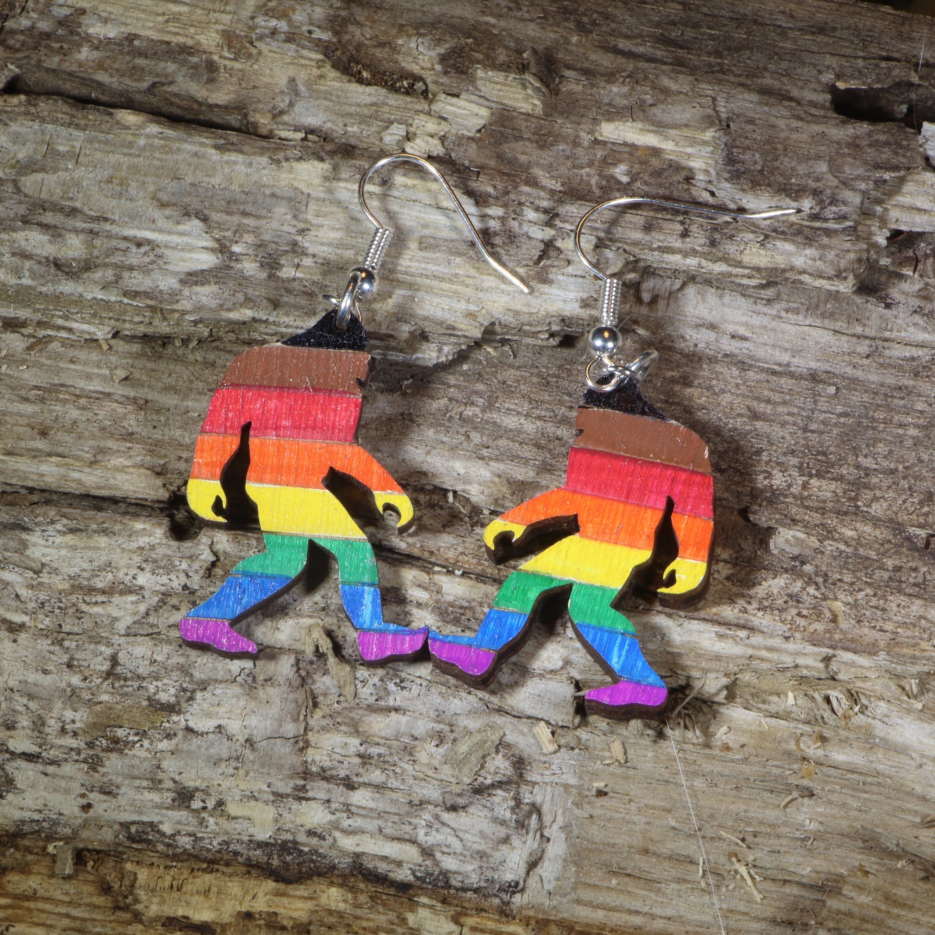 Hand-painted wooden rainbow pride Bigfoot dangle earrings featuring a colorful Sasquatch silhouette with rainbow stripes, hypoallergenic sterling silver hooks, and lightweight LGBTQ+ cryptid jewelry for pride celebrations and Bigfoot fans by Cate&