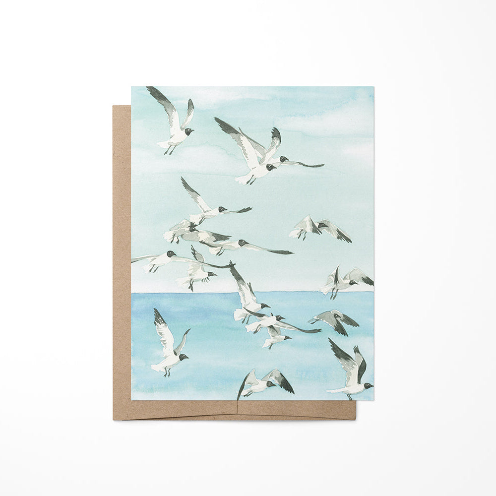A greeting card featuring a painting of seagulls flying at the beach, with a Kraft envelope.