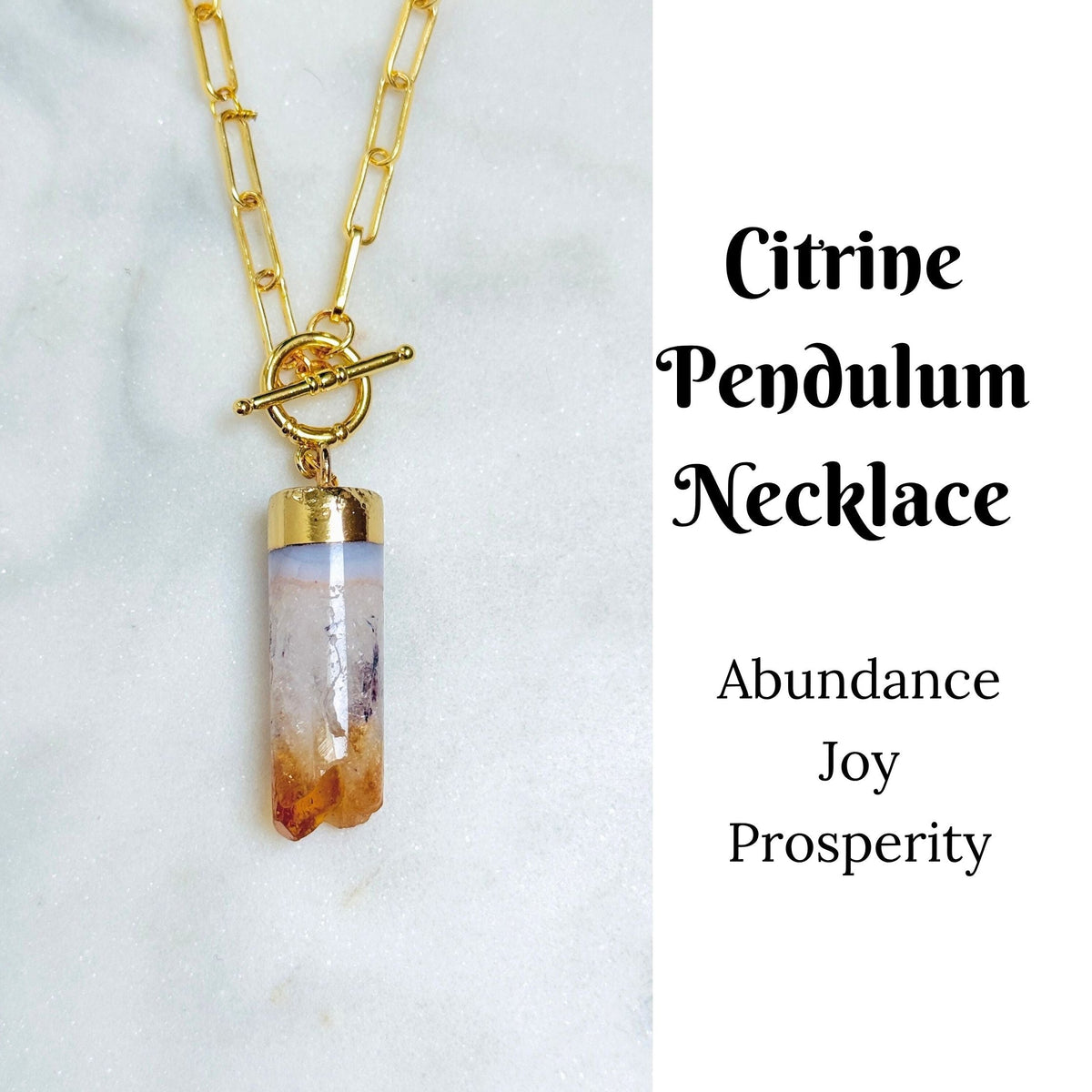 A gold-tone Citrine pendant necklace with a bar clasp and paperclip chain, displayed on a white marble surface next to text that reads &