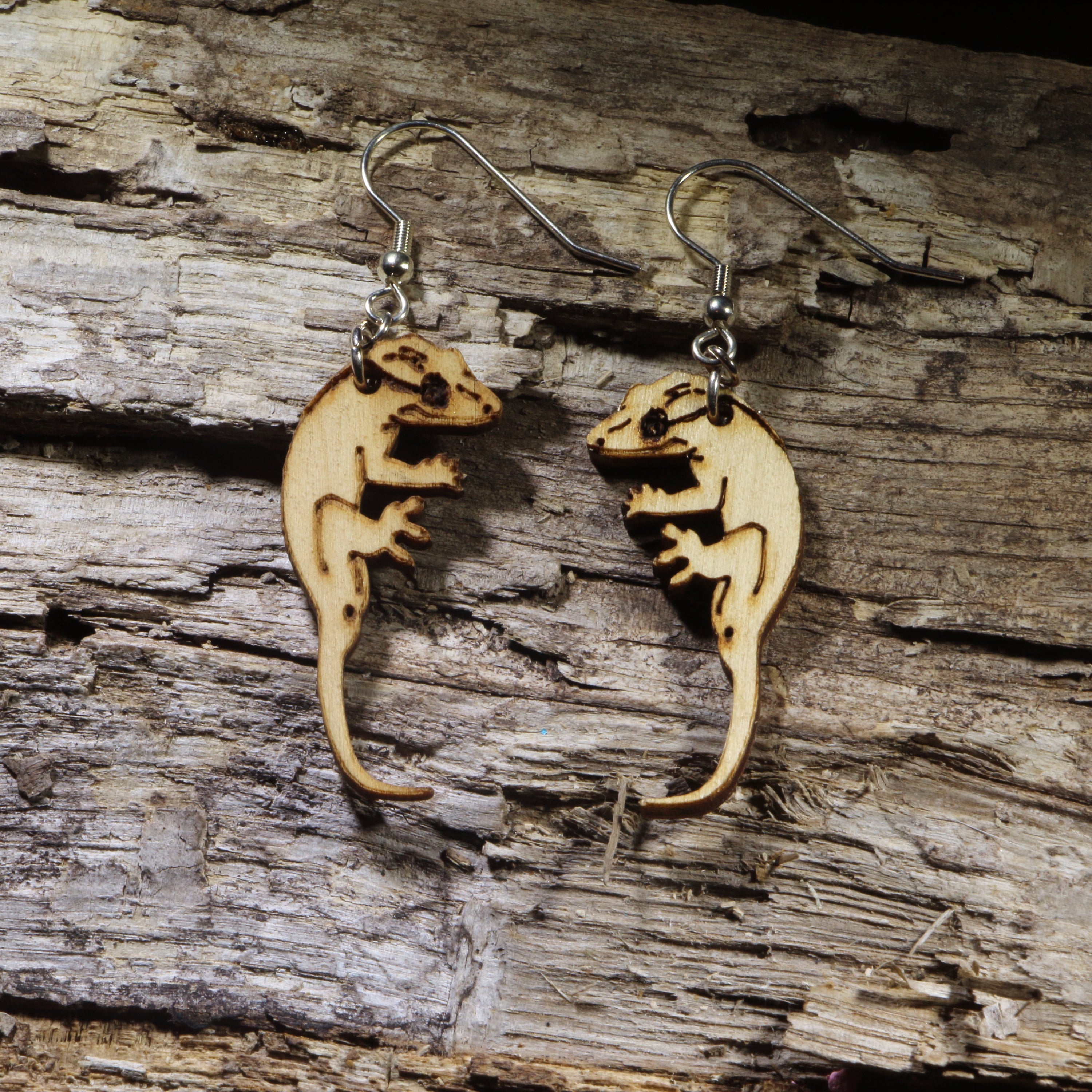 Hand-painted wooden crested gecko dangle earrings featuring a detailed gecko silhouette with curled tail and engraved accents. Lightweight reptile earrings with hypoallergenic .925 sterling silver hooks, perfect for crested gecko owners, reptile lovers, herpetology enthusiasts, exotic pet fans, and anyone who loves unique handmade animal jewelry.