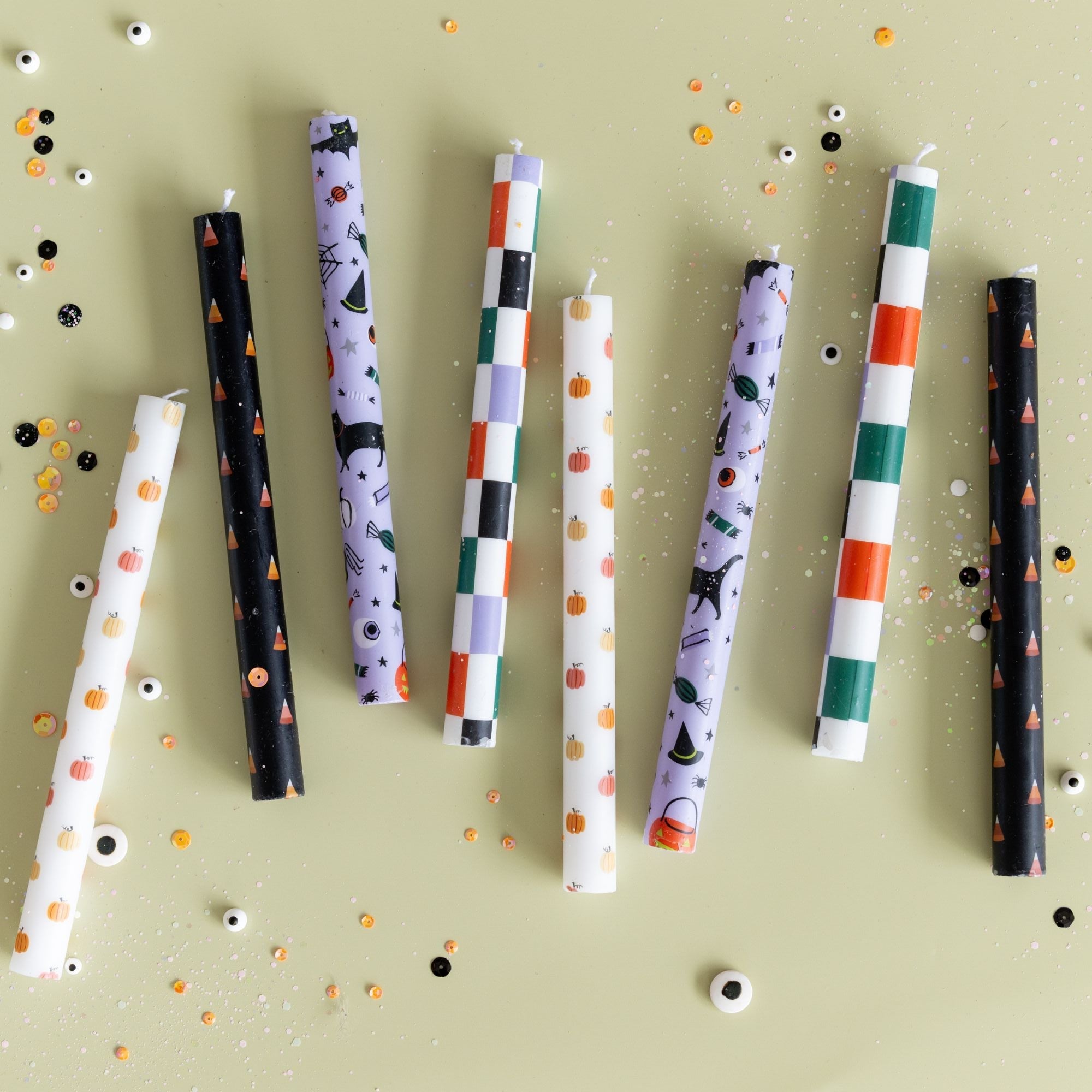 Assorted Halloween taper candles in checkered and printed patterns on green with confetti.