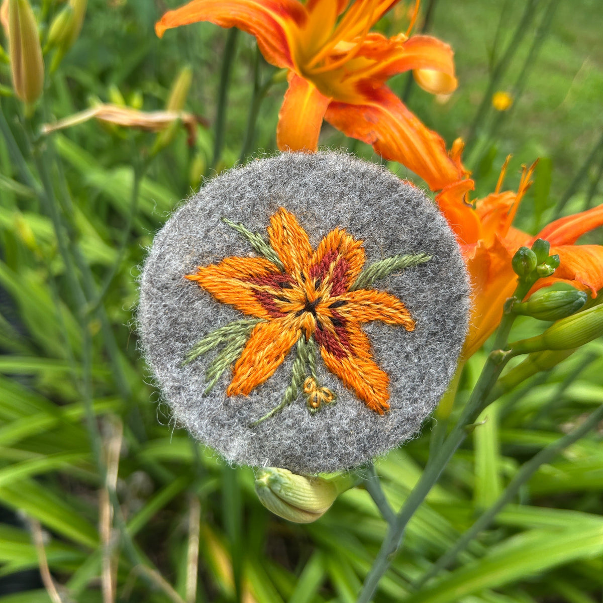 Embroidered day lily design on a textured gray surface with orange daylily in the background