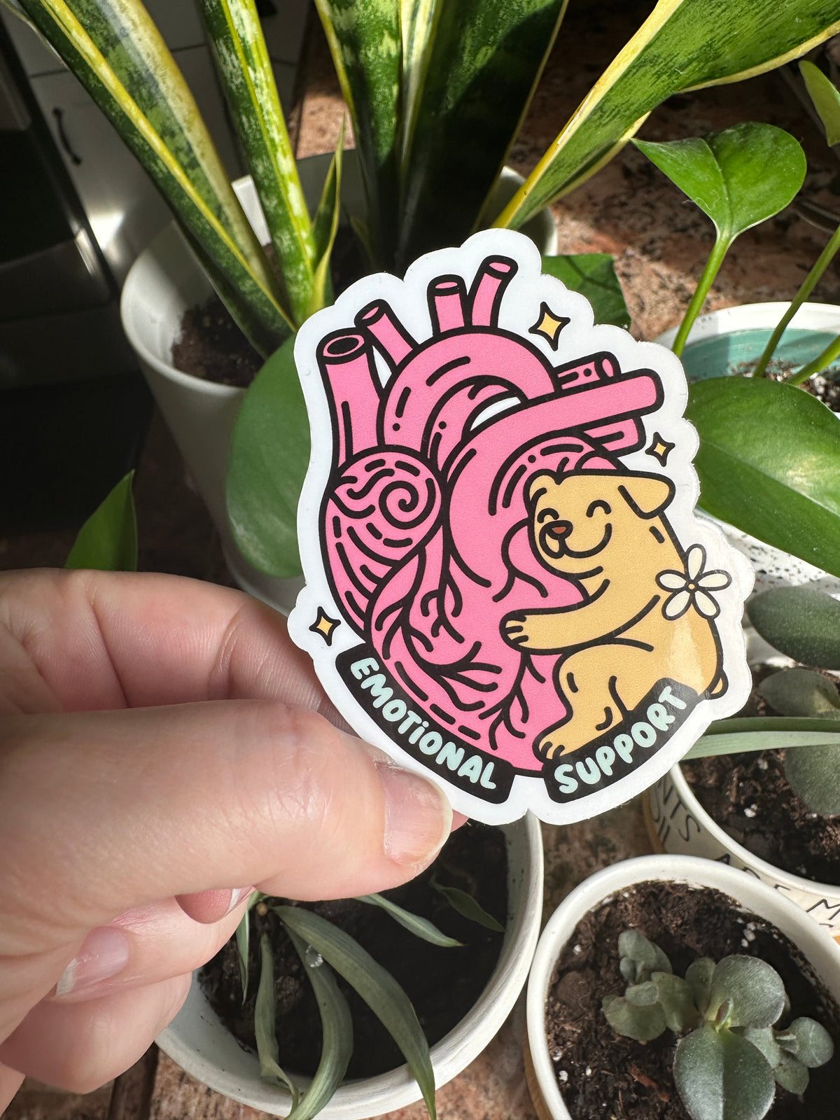 A hand holding a sticker with an illustration of a dog and a heart, with the text &