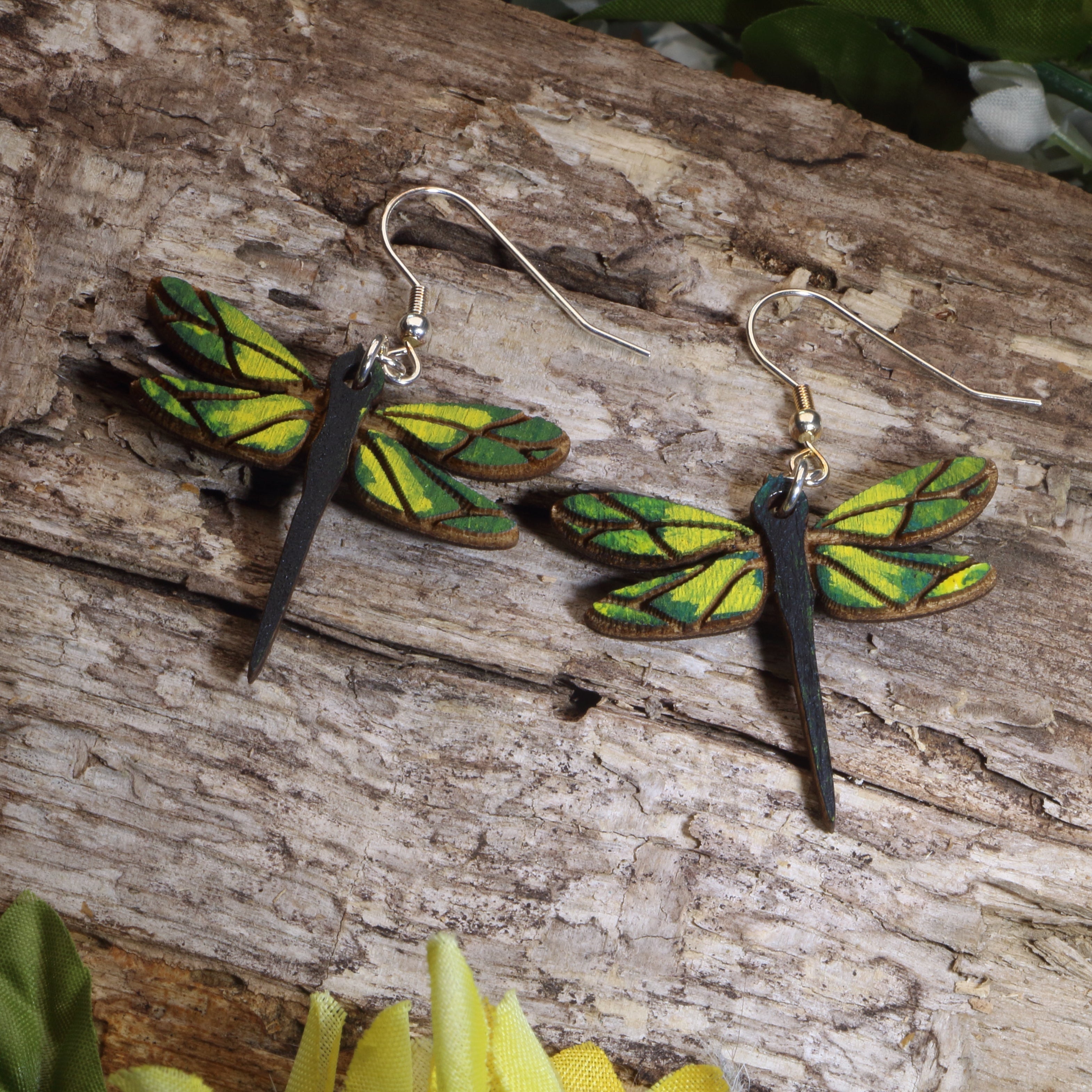 Dragonfly-shaped earrings on a wooden surface with green leaves.