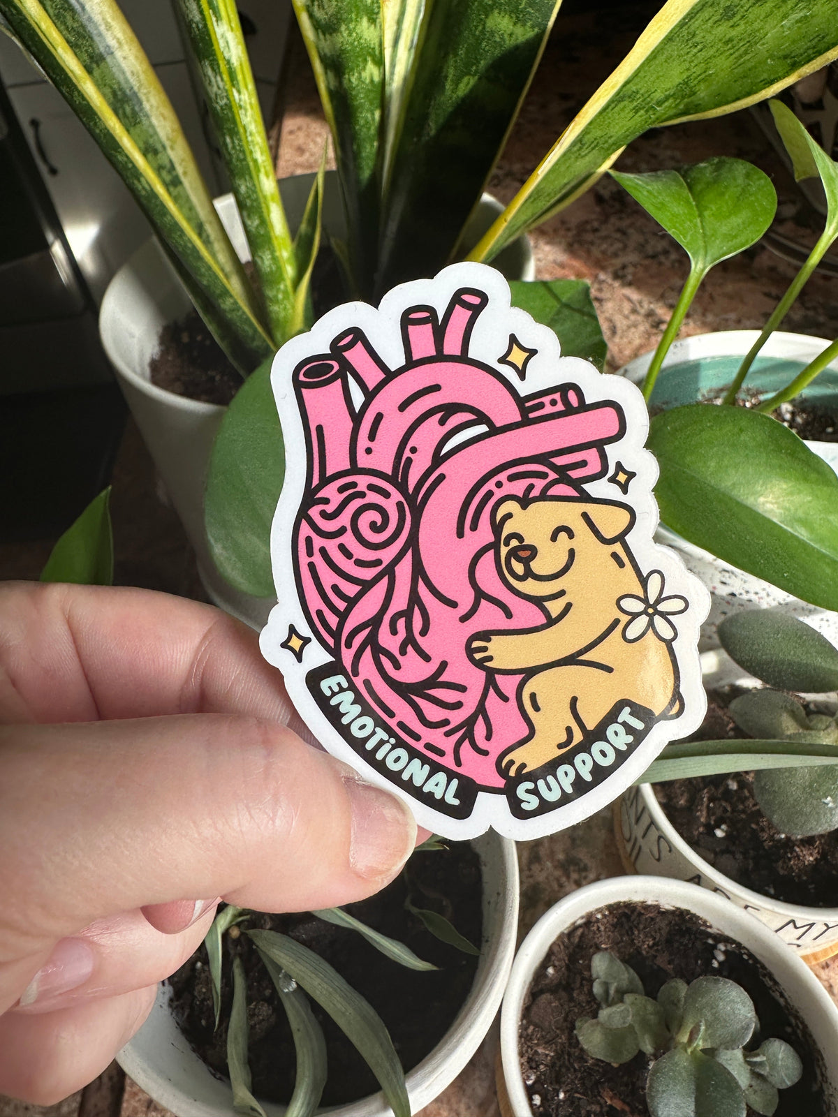 A hand holding a sticker with an illustration of a dog and a heart, with the text &