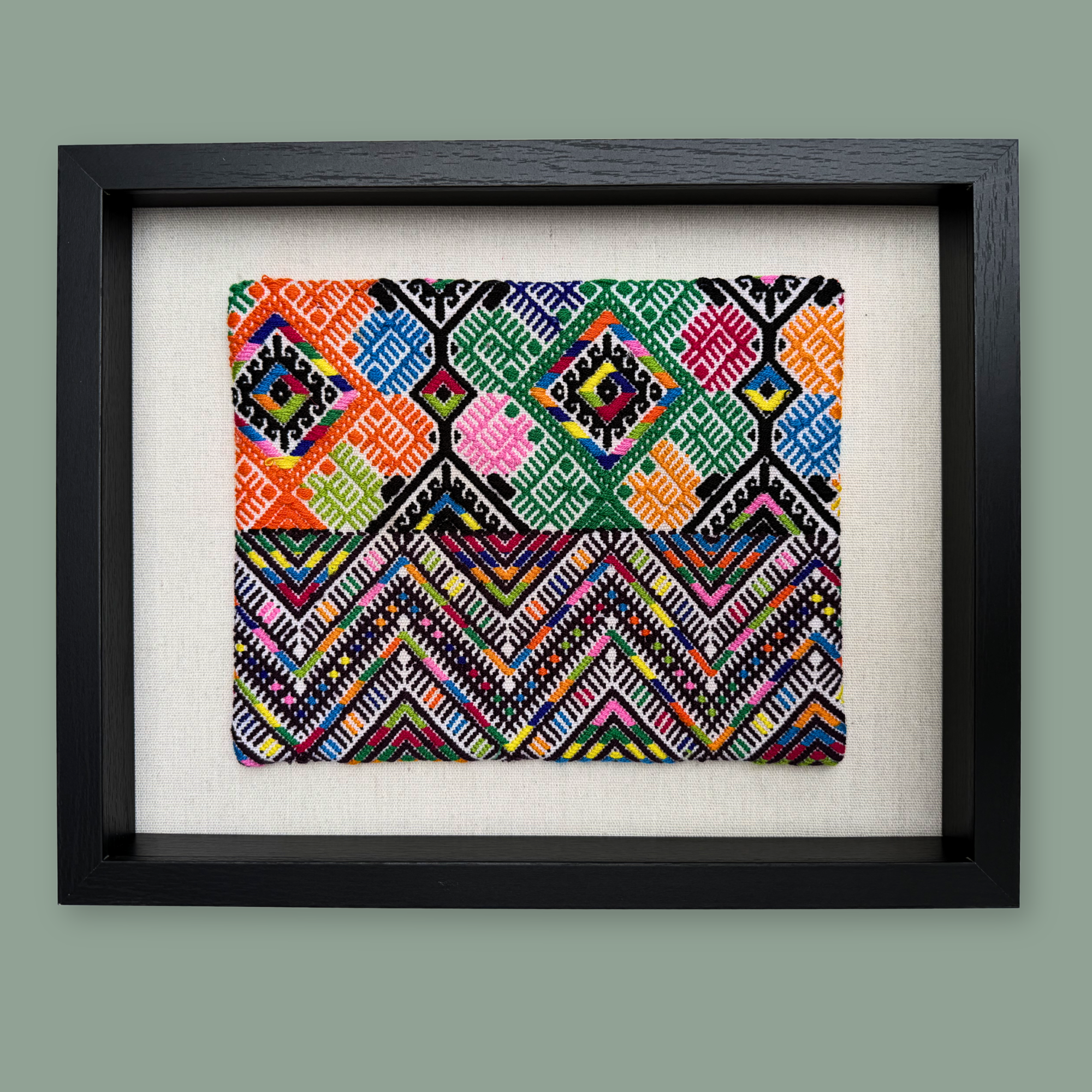 Framed vintage huipil textile with a colorful geometric pattern on a light background
