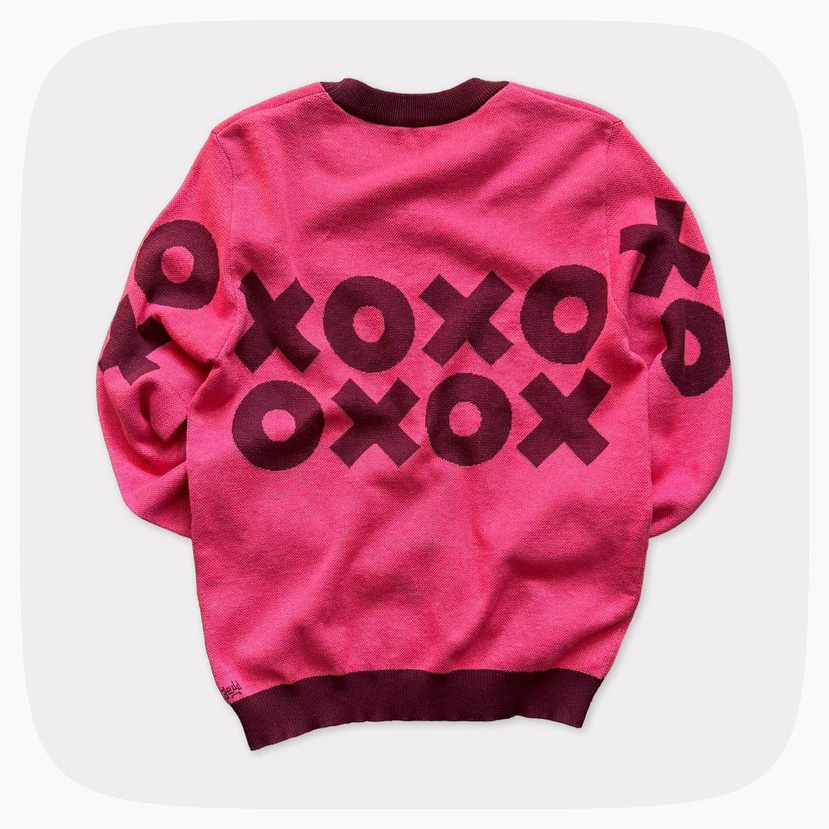 The back view of A pink graphic knit sweater with a dark red XOXO pattern across the chest.