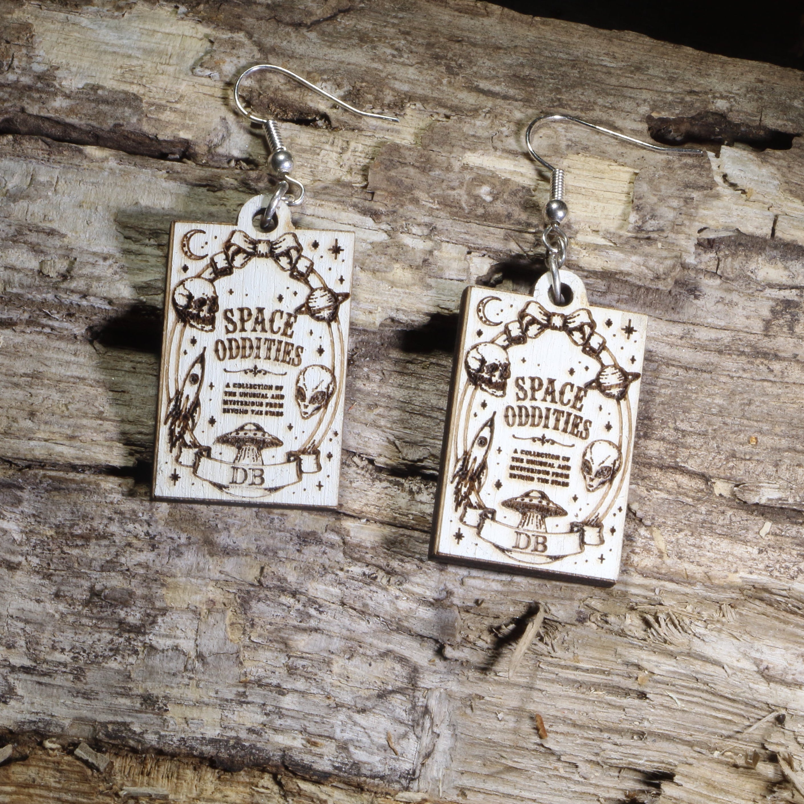 Hand-painted wooden Space Oddities book cover dangle earrings featuring a vintage-inspired sci-fi gothic book cover design on hypoallergenic .925 sterling silver hooks. Lightweight book lover jewelry for readers, science fiction fans, gothic literature enthusiasts, horror lovers, librarians, and collectors of unique literary accessories.