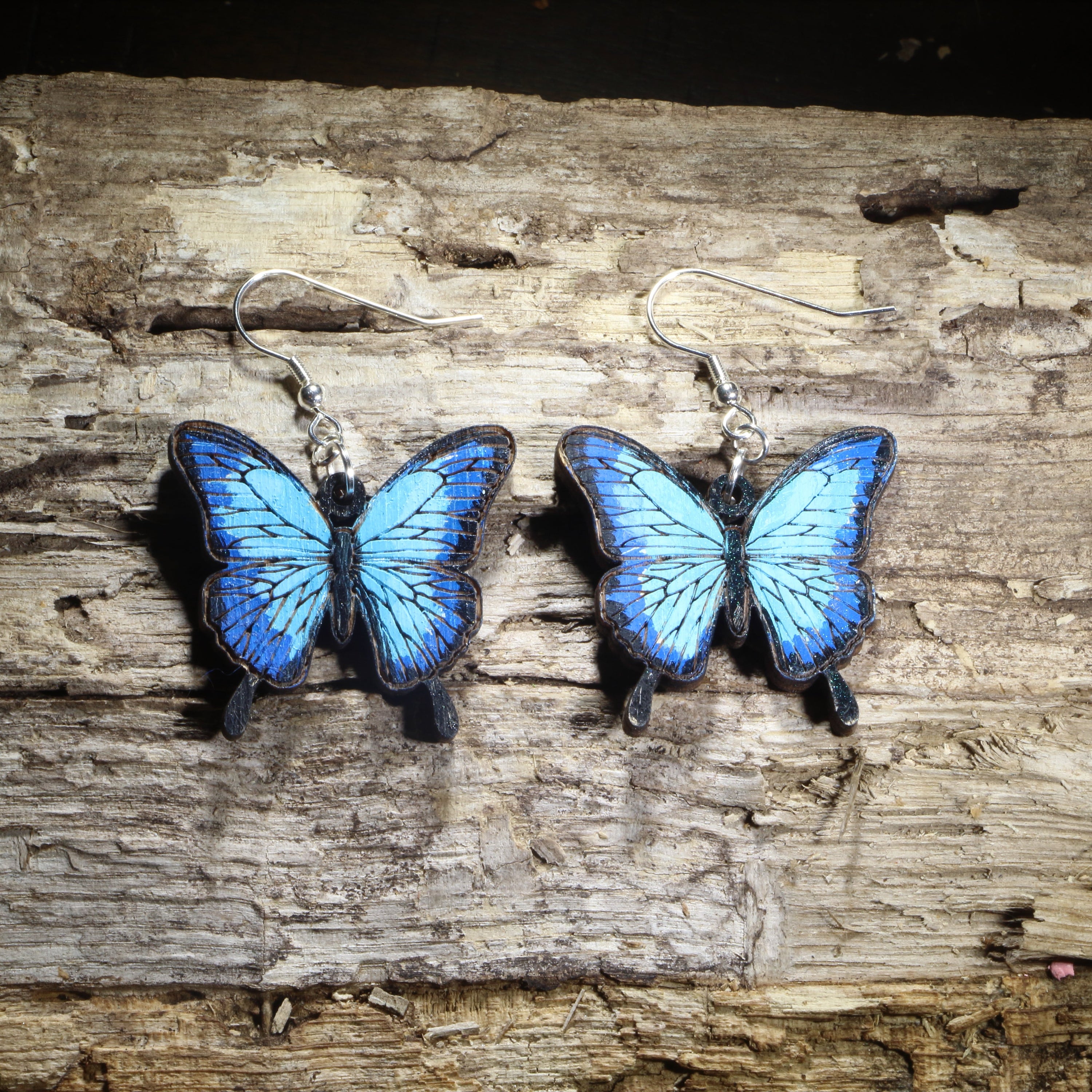 Hand-painted wooden blue morpho butterfly dangle earrings featuring vibrant blue butterfly wings with realistic black edging on hypoallergenic .925 sterling silver hooks. Lightweight butterfly jewelry for nature lovers, gardeners, butterfly enthusiasts, pollinator supporters, and anyone who loves colorful insect-inspired accessories.