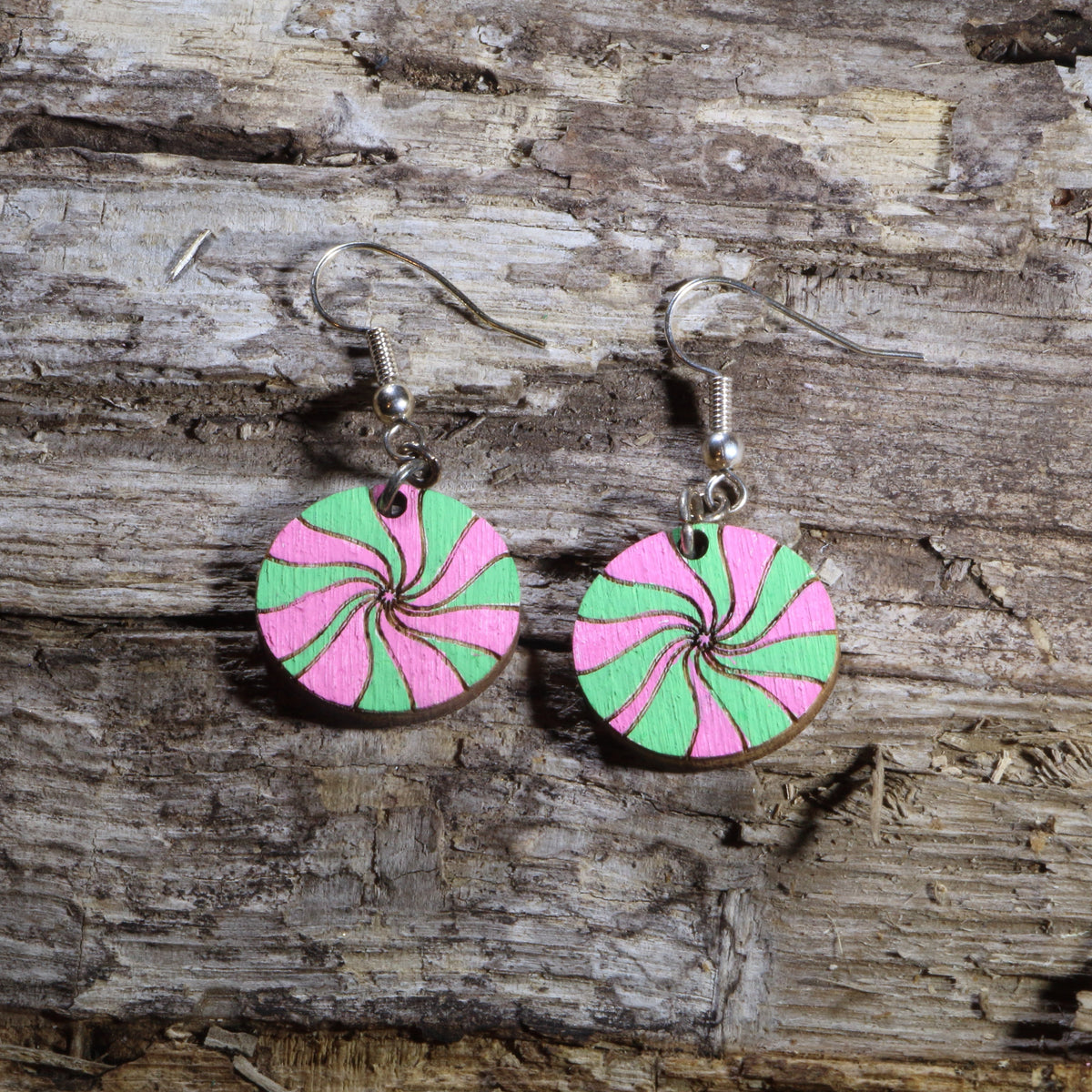 Hand-painted wooden pink and green peppermint candy dangle earrings featuring festive swirled Christmas candies in bright holiday colors. Lightweight Christmas earrings with hypoallergenic .925 sterling silver hooks, perfect for holiday parties, candy lovers, winter celebrations, stocking stuffers, and cheerful festive outfits.