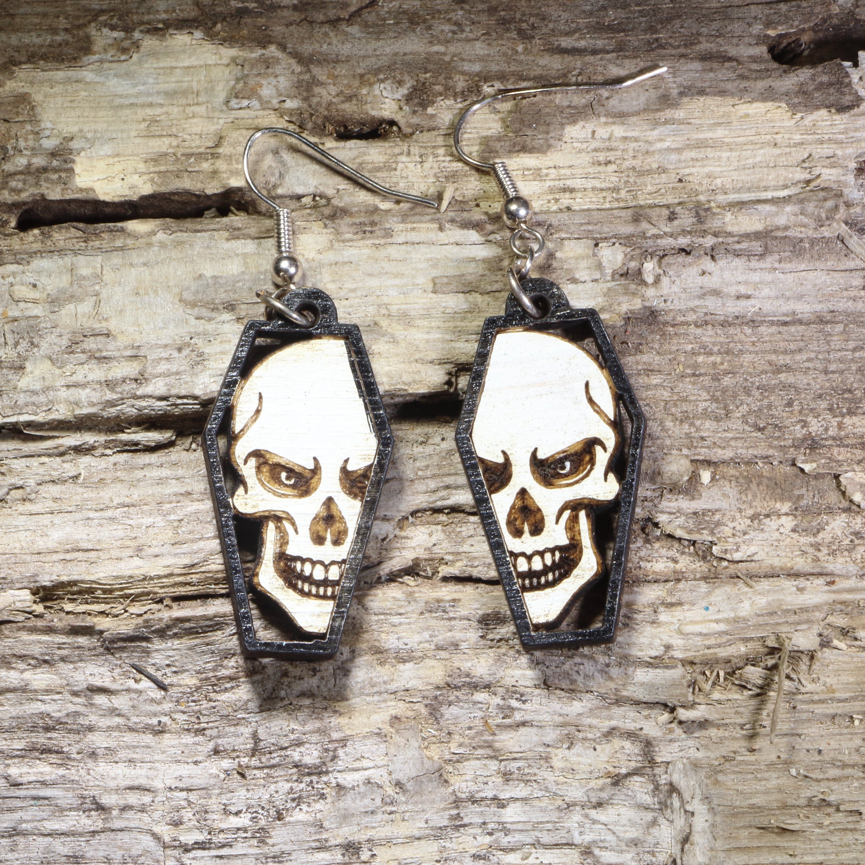 Hand-painted wooden skull in coffin dangle earrings featuring a detailed gothic skull framed inside a black coffin on hypoallergenic .925 sterling silver hooks. Lightweight gothic jewelry for Halloween, spooky style, horror fans, alternative fashion, and skull lovers.
