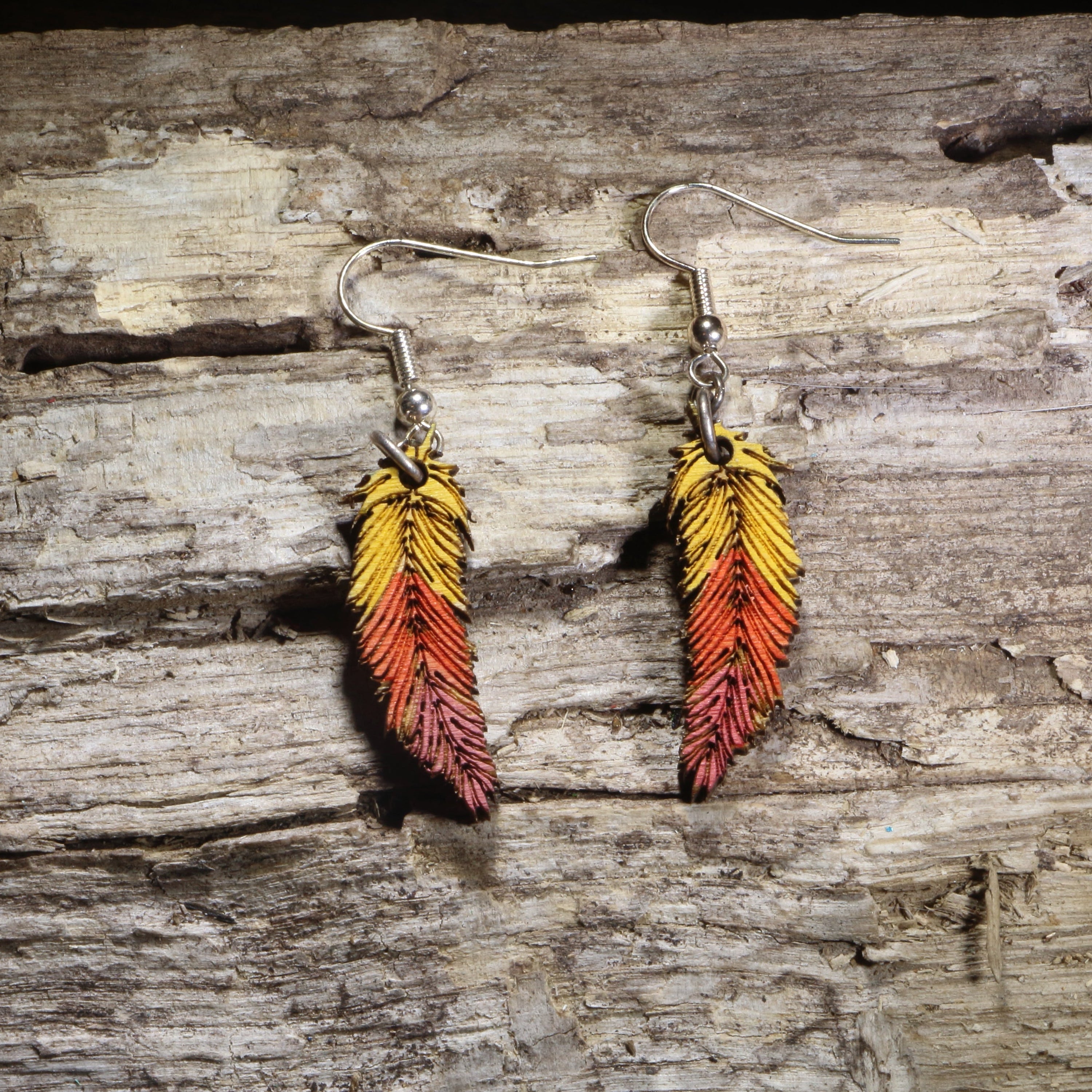 Handcrafted ombré feather wooden dangle earrings featuring hand-painted yellow, orange, and red gradient feathers with engraved detailing. Lightweight laser-cut wooden earrings with hypoallergenic .925 sterling silver hooks, perfect for boho fashion, autumn accessories, nature lovers, festival wear, and colorful handcrafted jewelry.