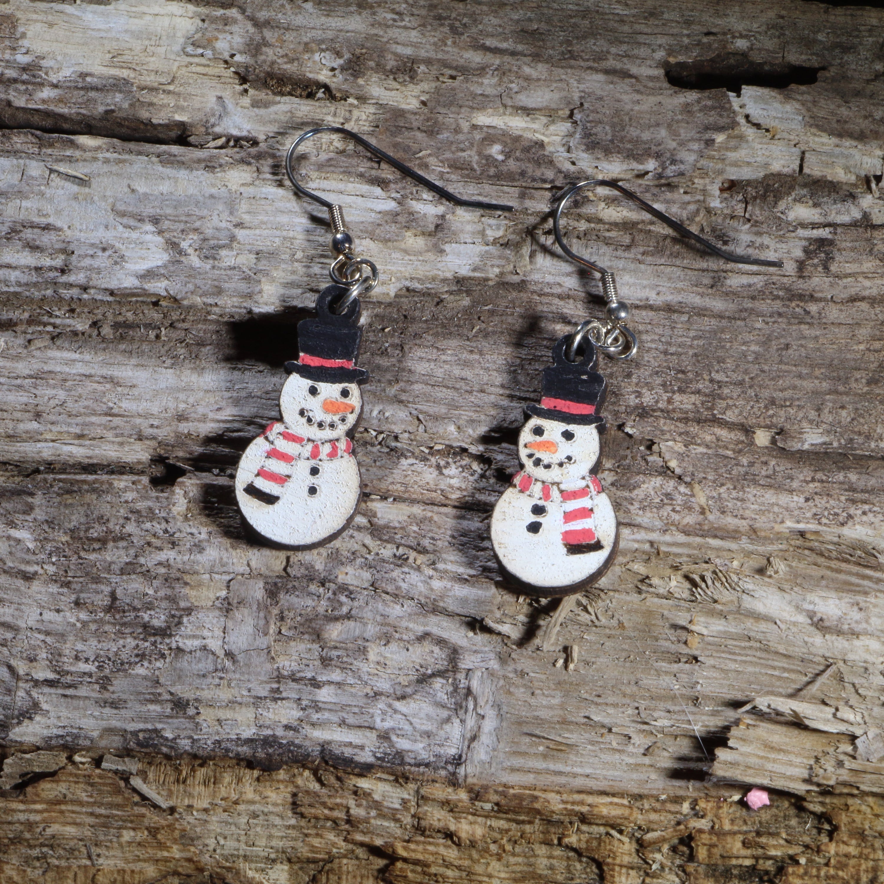 Handcrafted wooden snowman dangle earrings featuring cheerful snowmen with black top hats, red striped scarves, and carrot noses. These lightweight Christmas earrings are finished with hypoallergenic .925 sterling silver hooks, making them a festive accessory for holiday parties, winter celebrations, Christmas outfits, and seasonal gift giving.