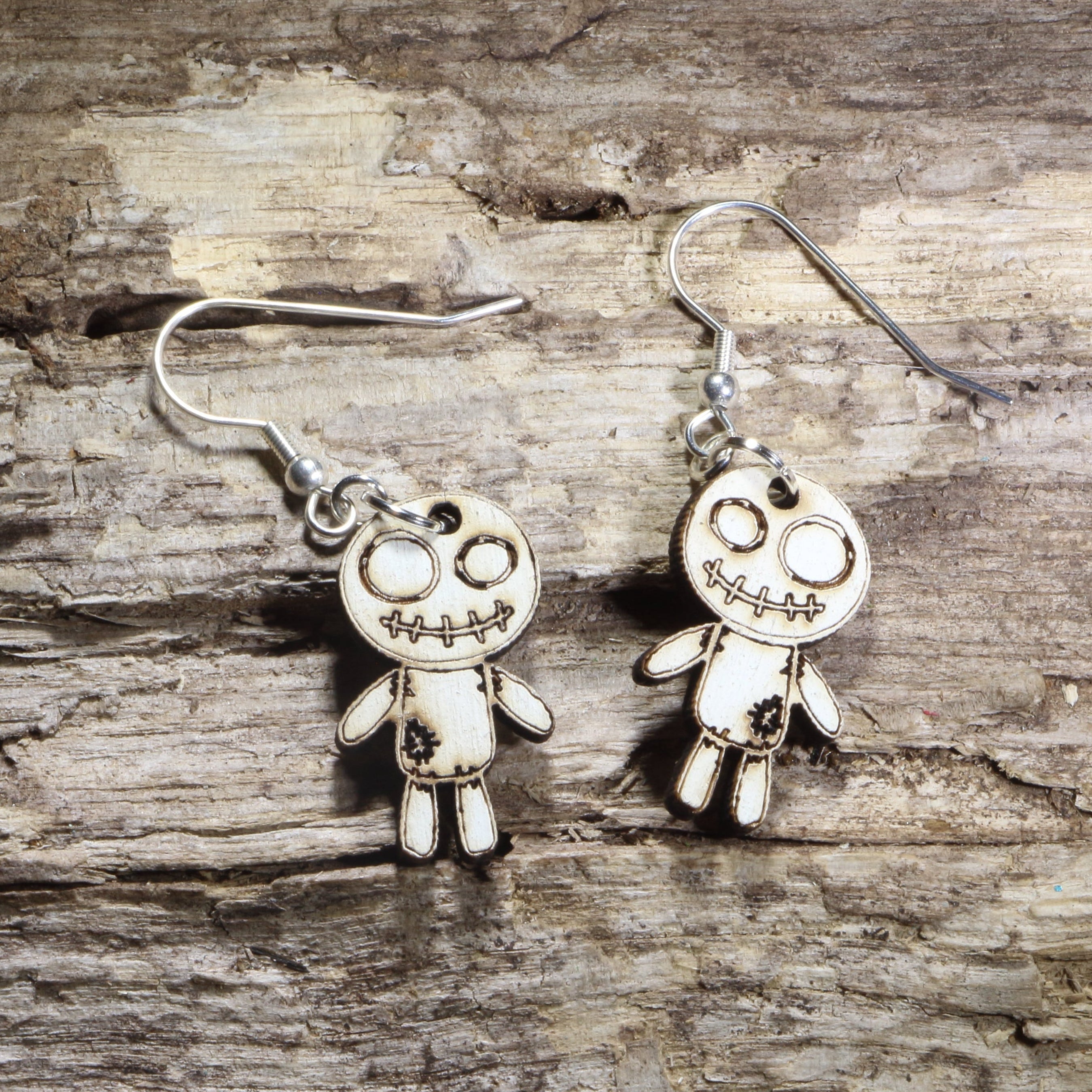 Handmade wooden voodoo doll dangle earrings featuring a stitched rag doll design with oversized eyes and patch details. Lightweight gothic-inspired earrings crafted from wood with hypoallergenic .925 sterling silver hooks, perfect for Halloween, spooky style, horror fans, gothic fashion, and lovers of creepy cute jewelry.
