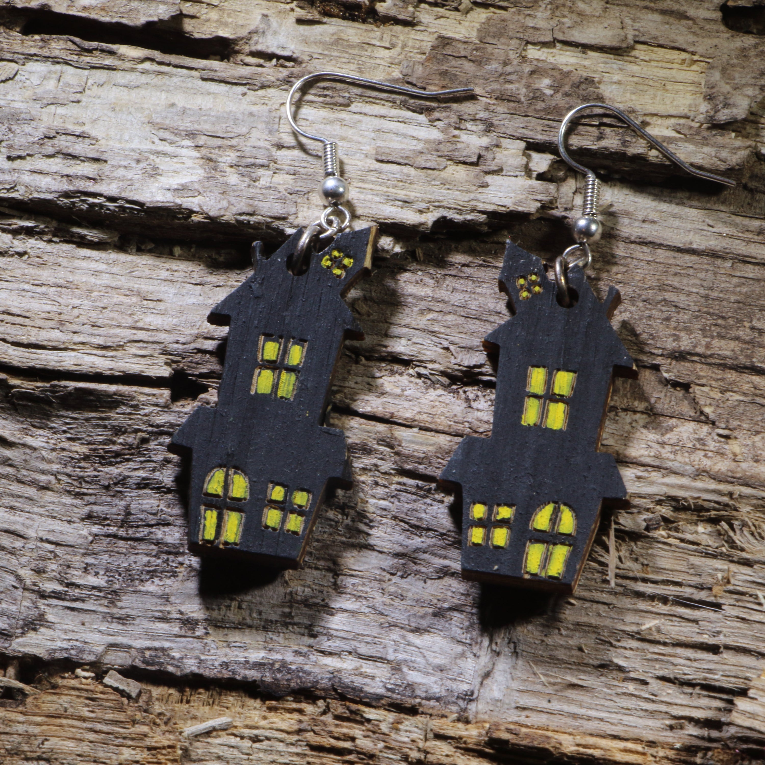 Hand-painted wooden haunted house dangle earrings featuring a spooky black house with glowing yellow windows. Lightweight Halloween earrings with hypoallergenic .925 sterling silver hooks, perfect for haunted house fans, spooky season, Halloween parties, ghost tours, and anyone who loves eerie Halloween jewelry.