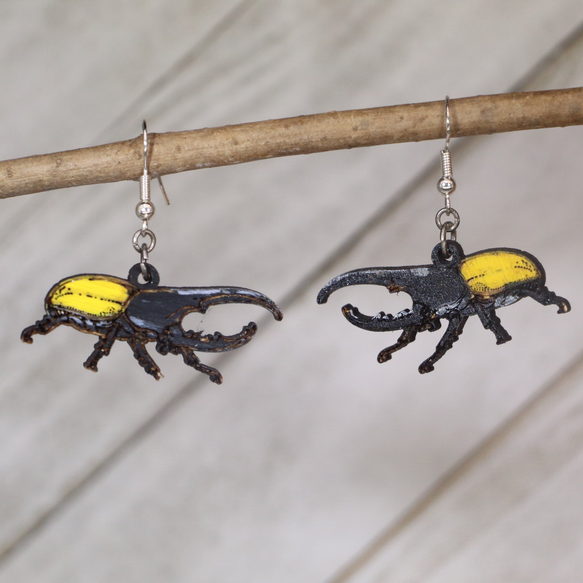 Pair of beetle-shaped earrings on a branch against a neutral background