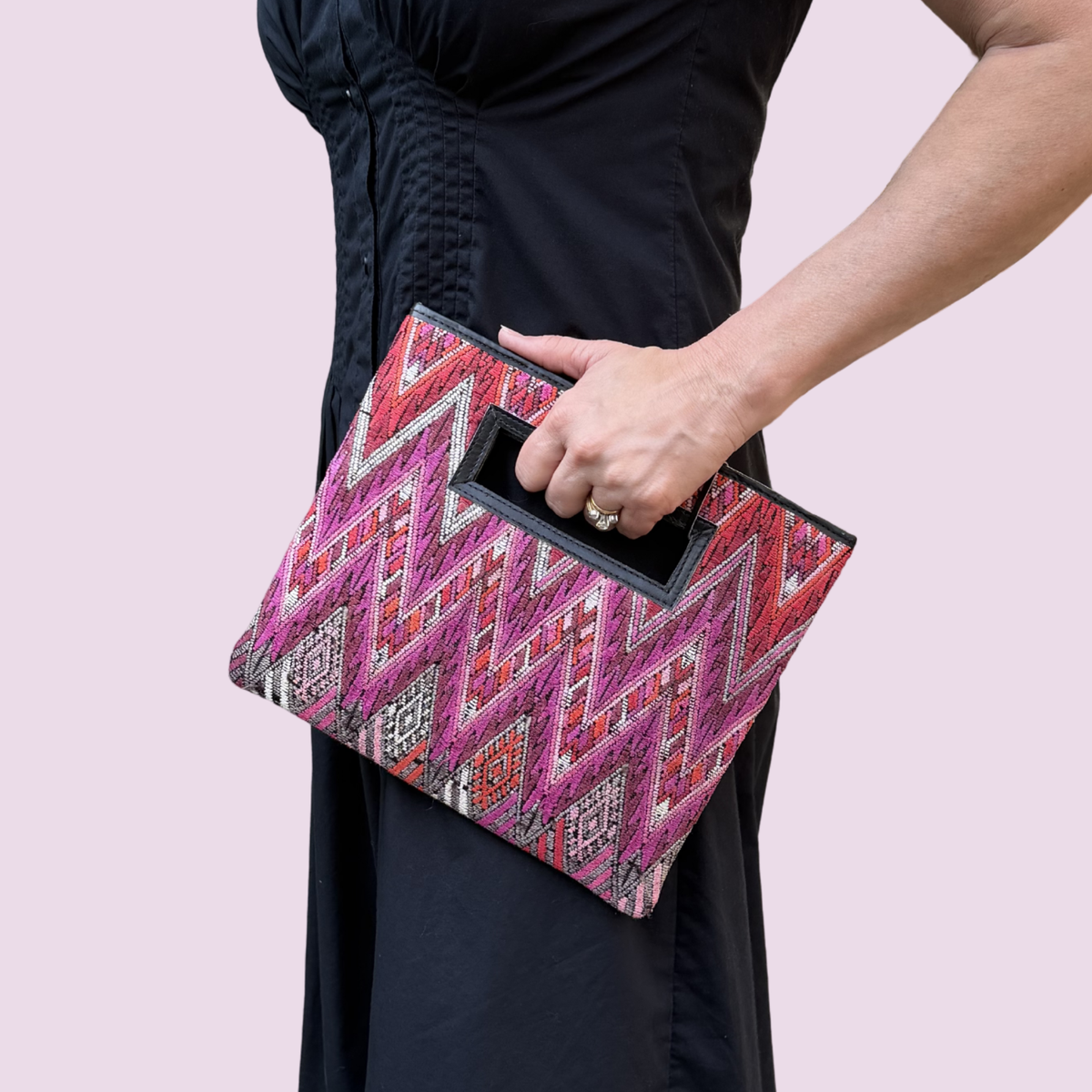 Person holding a pink and black patterned clutch bag against a light pink background