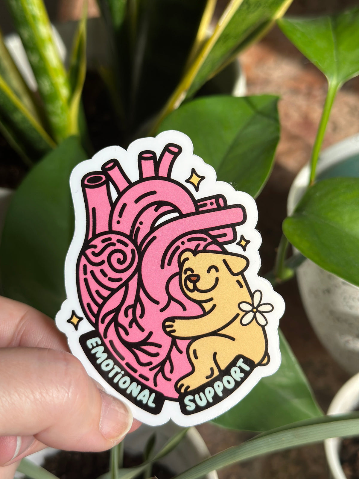 A hand holding a sticker with an illustration of a dog and a heart, with the text &