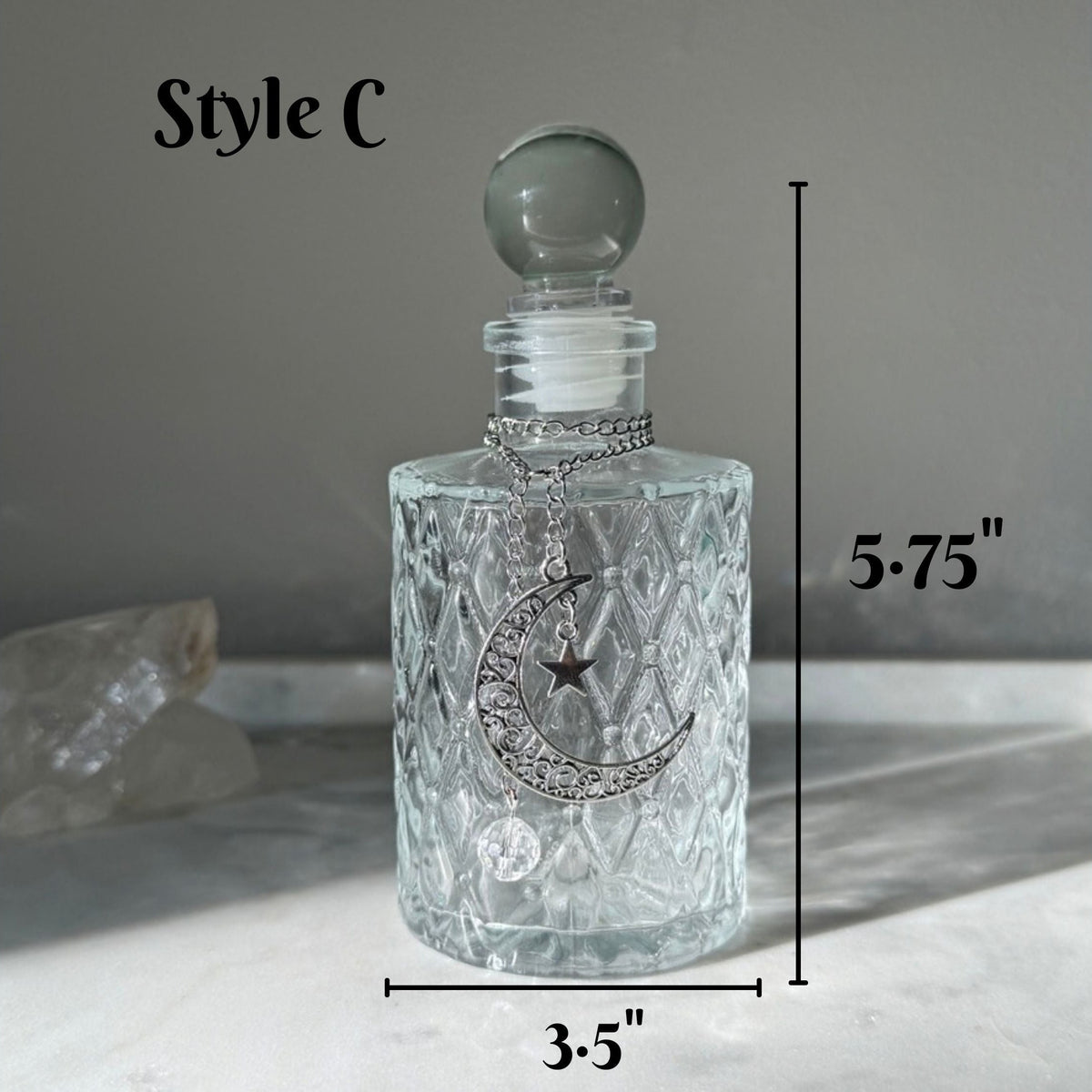 A clear glass decanter with a textured diamond pattern, a silver crescent moon and star design on the front, and a round glass stopper. The image includes dimension lines indicating a height of 5.