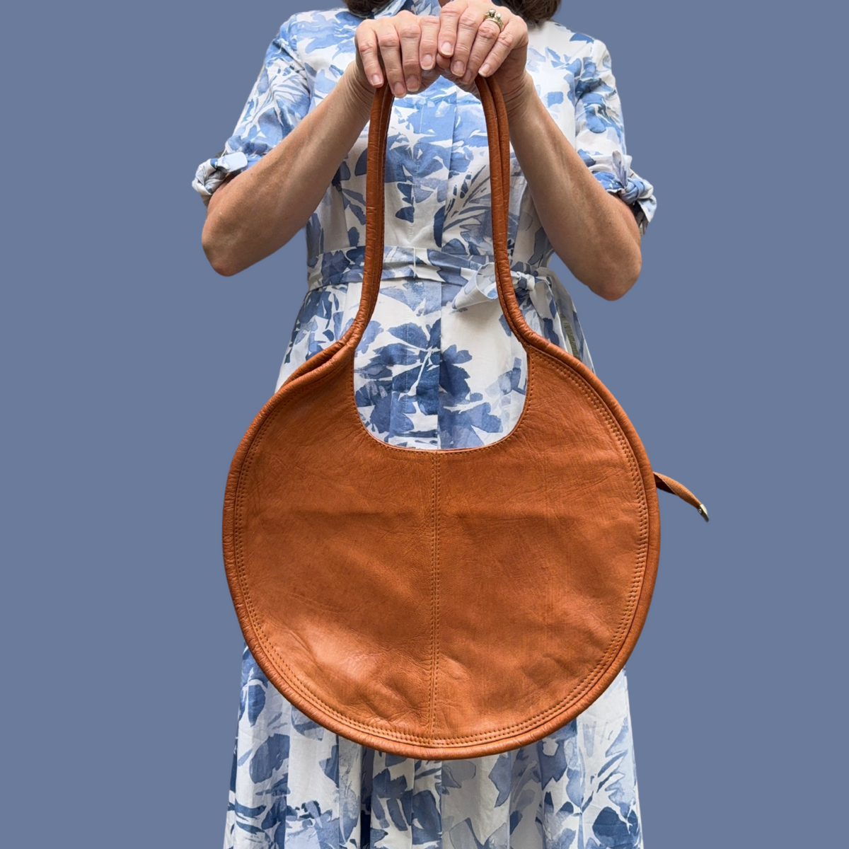 Person holding a brown leather circular-shaped handbag against a plain background