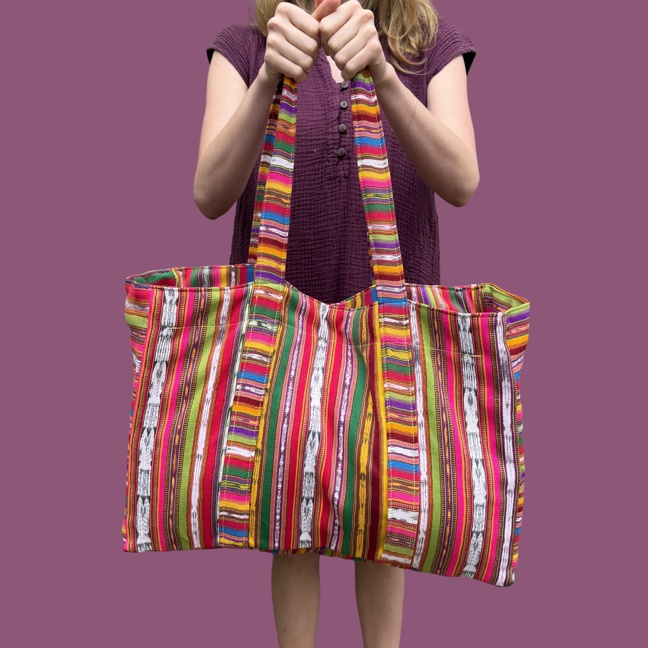 Person holding a colorful striped tote bag against a purple background