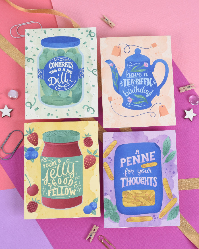 A set of four folded greeting cards with colorful illustrations and text on them, displayed against a background with decorative stars and a background paper with a pink and purple gradient.