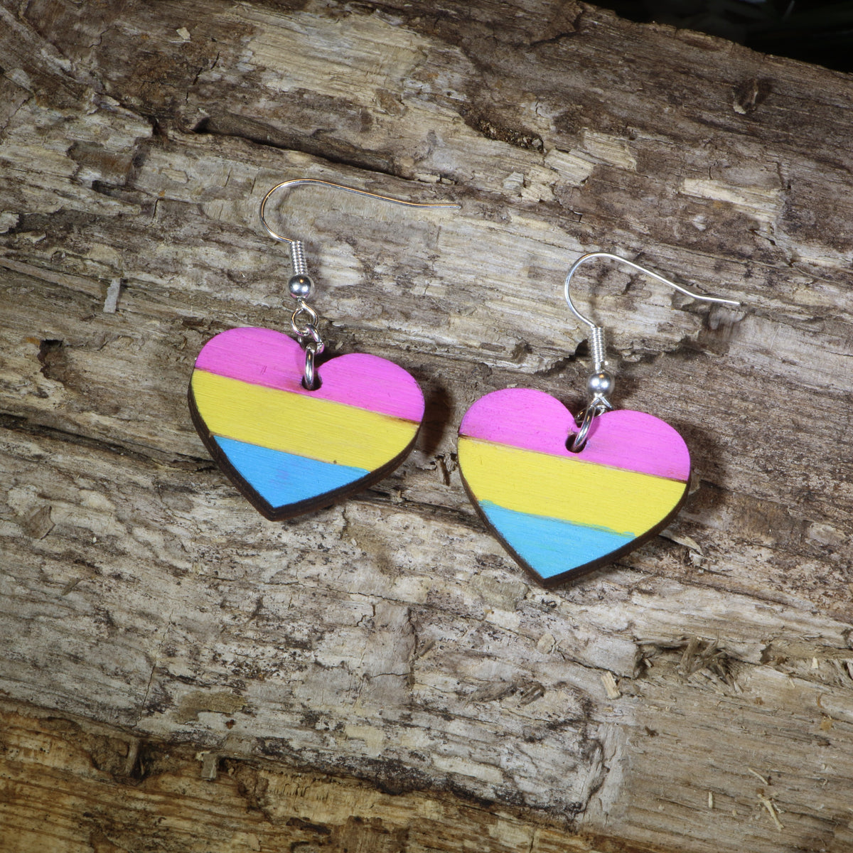 Hand-painted wooden pansexual heart dangle earrings featuring pink, yellow, and blue pansexual pride stripes, hypoallergenic sterling silver hooks, and lightweight LGBTQ+ pride jewelry for pansexual pride celebrations and queer accessory lovers by Cate&